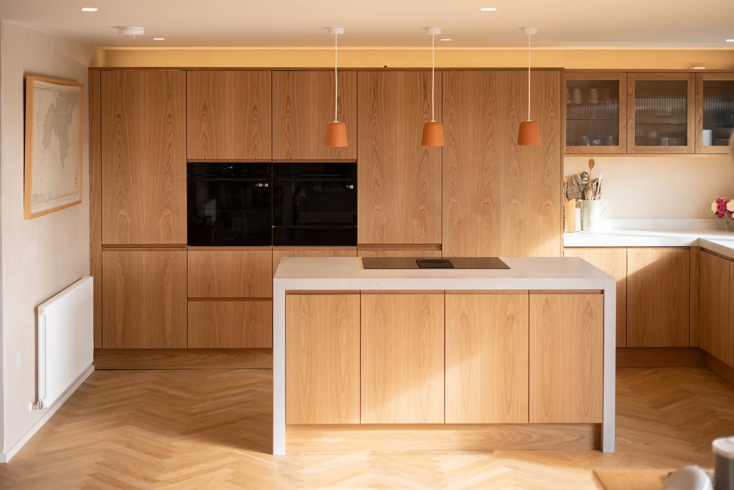 Modern kitchen with wooden cabinets, a white kitchen island, and hanging orange pendant lights.