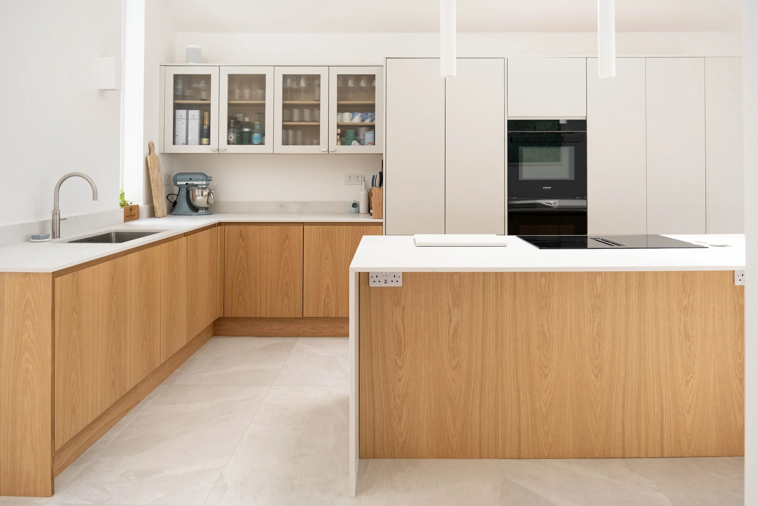 A modern kitchen with white and wood cabinetry, a kitchen island, built-in oven, and pendant lights.