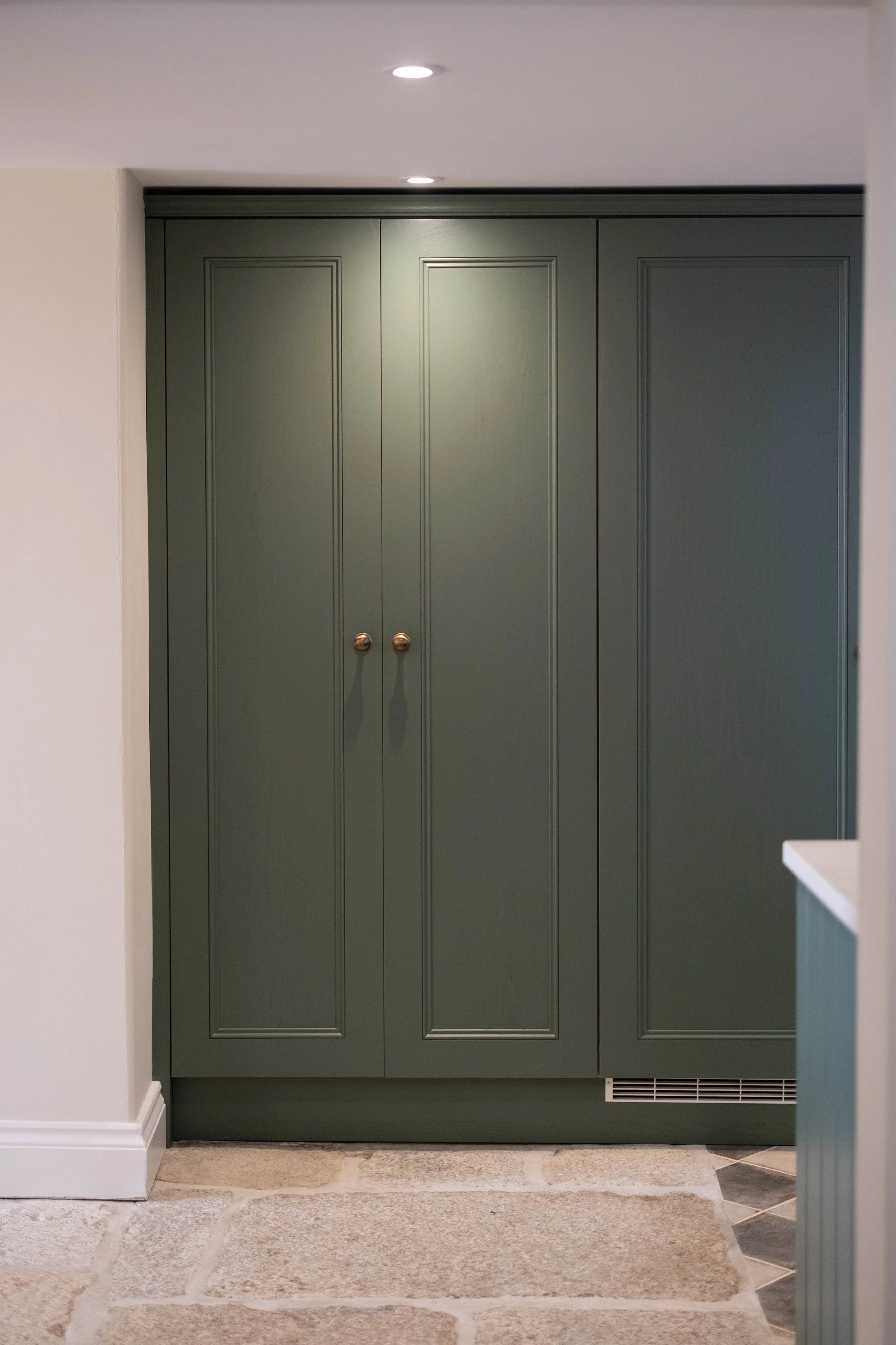 Green cabinet with gold knobs in a room with beige stone flooring, white walls, and a vent near the bottom.