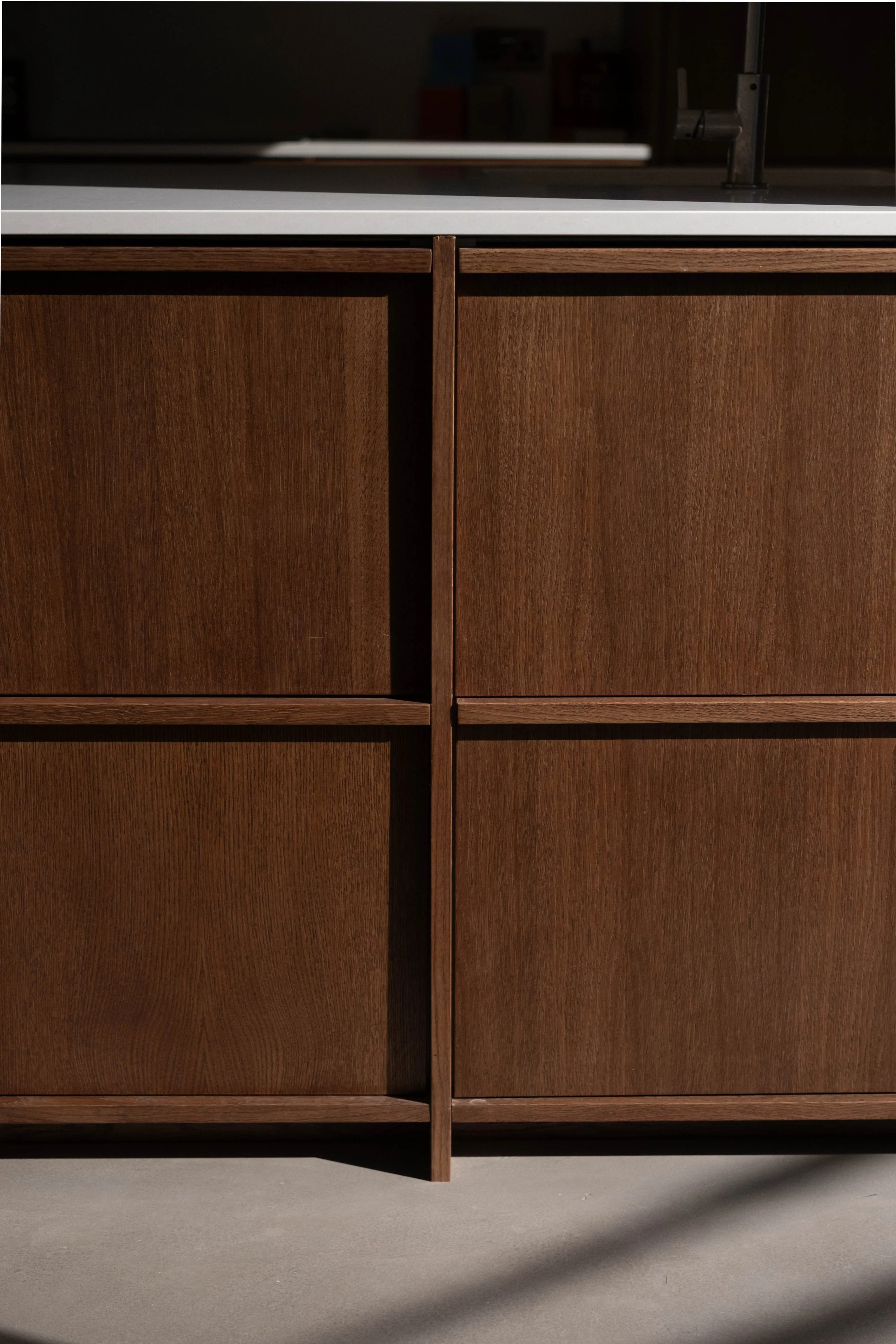 Close-up of a wooden cabinet with a dark finish, featuring four panels and a vertical divider in the middle, set against a gray concrete floor with a shadow underneath.