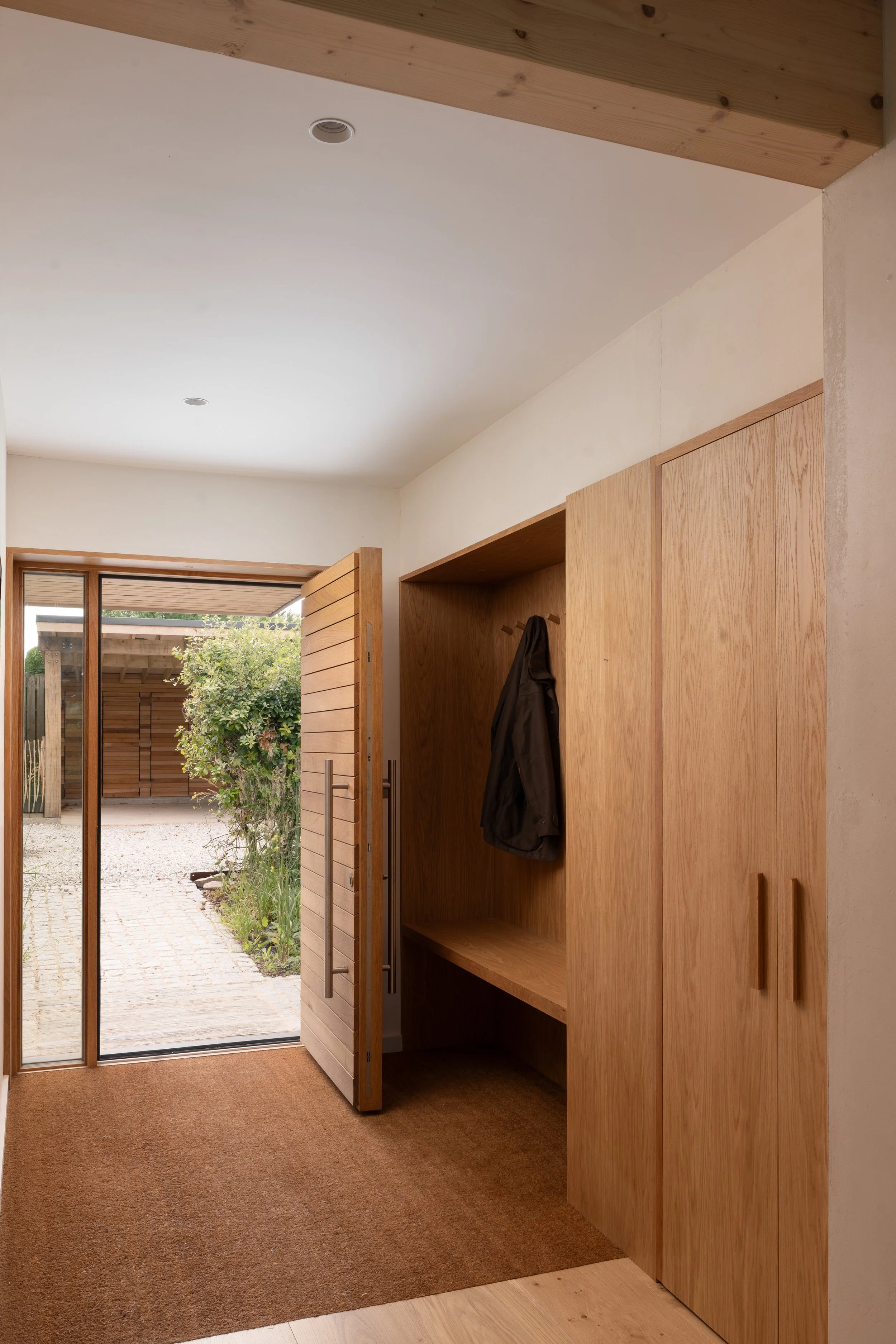 The image shows a doorway leading outside to a patio with a tree and wooden fence. Inside, there are wooden cabinets and a coat hanging on a hook.