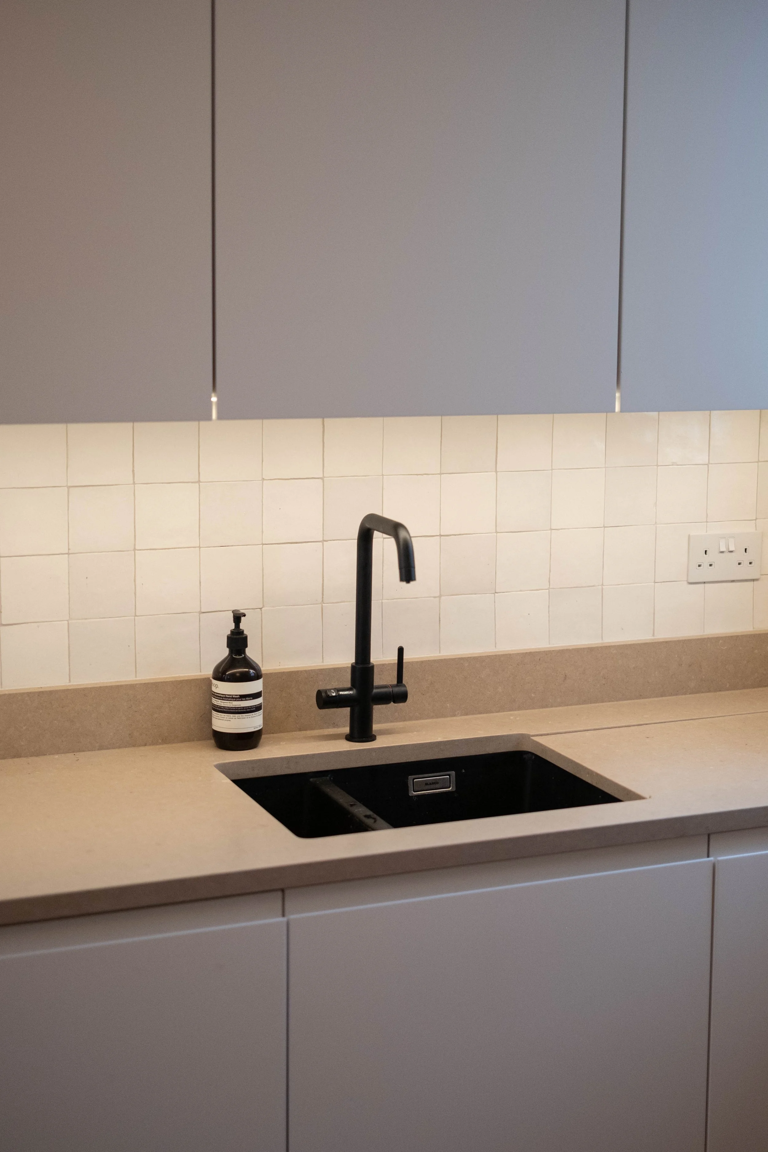 Kitchen sink with a black faucet, a bottle of hand soap, and a tiled backsplash with electrical outlets.