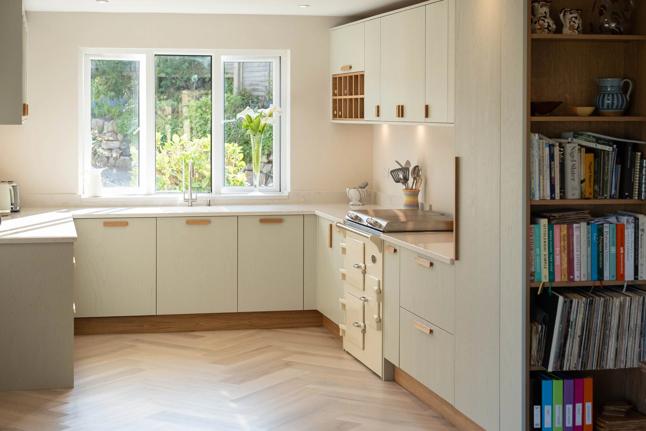 Kitchen with white cabinetry, a window with a garden view, and a bookshelf filled with cookbooks and decorative items.