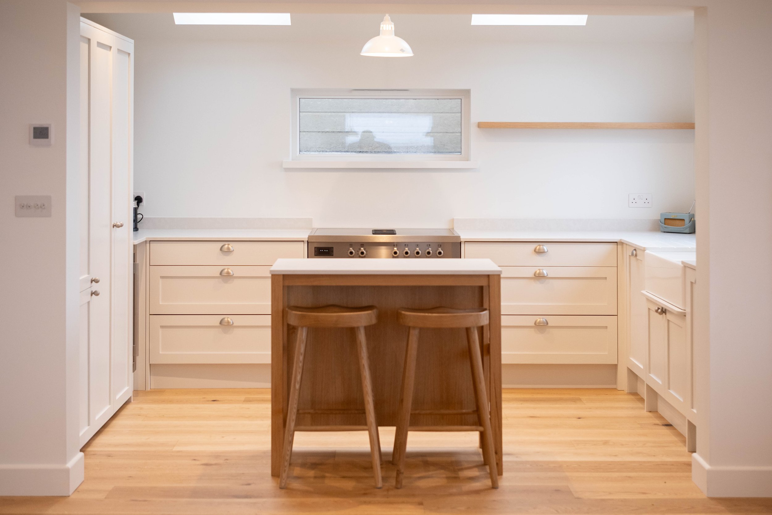 Modern kitchen with white cabinets, a central island with wooden chairs, a window above the stove, and a skylight ceiling.
