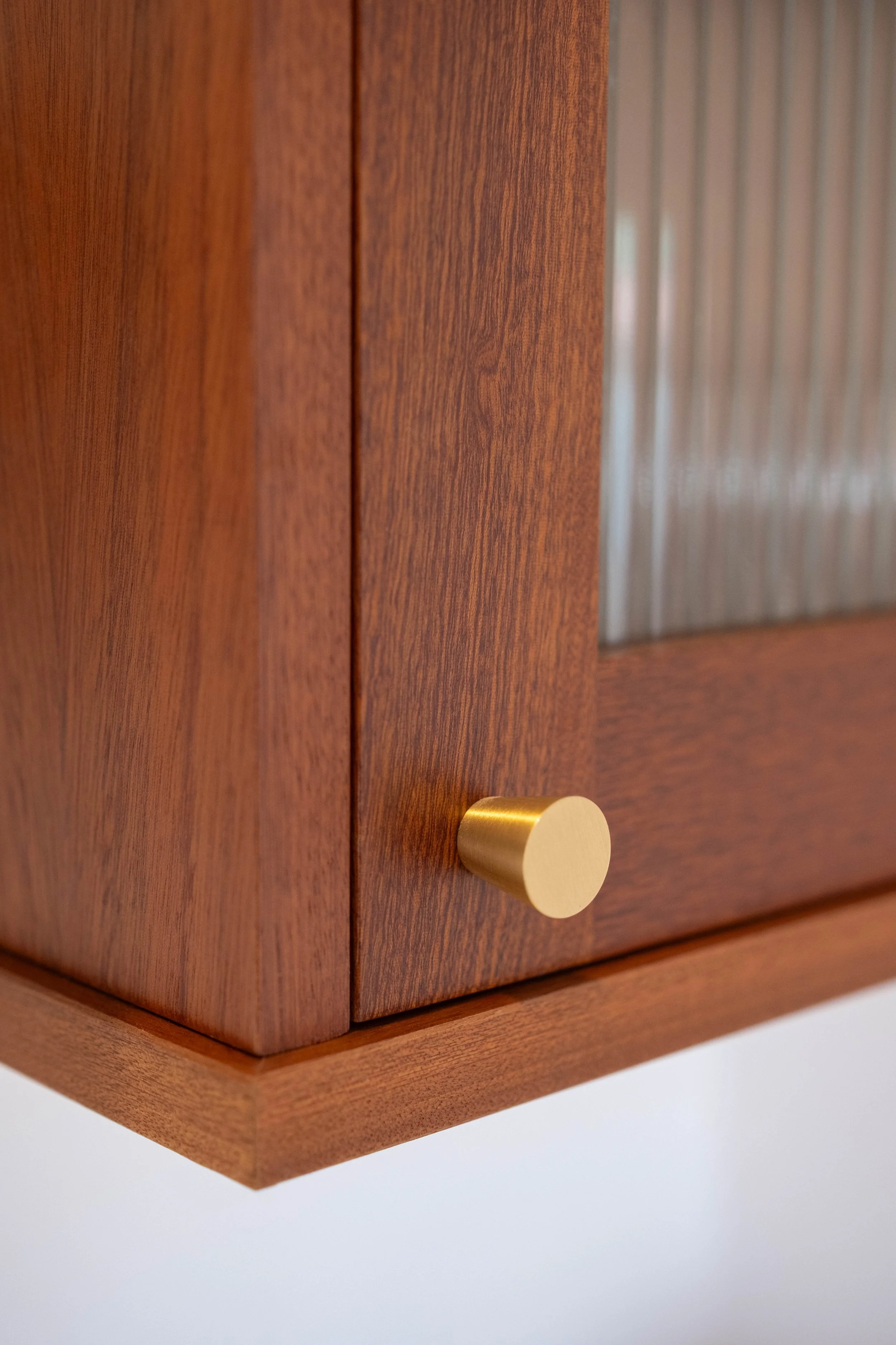 A wooden cabinet with a gold knob and a glass panel on the door.