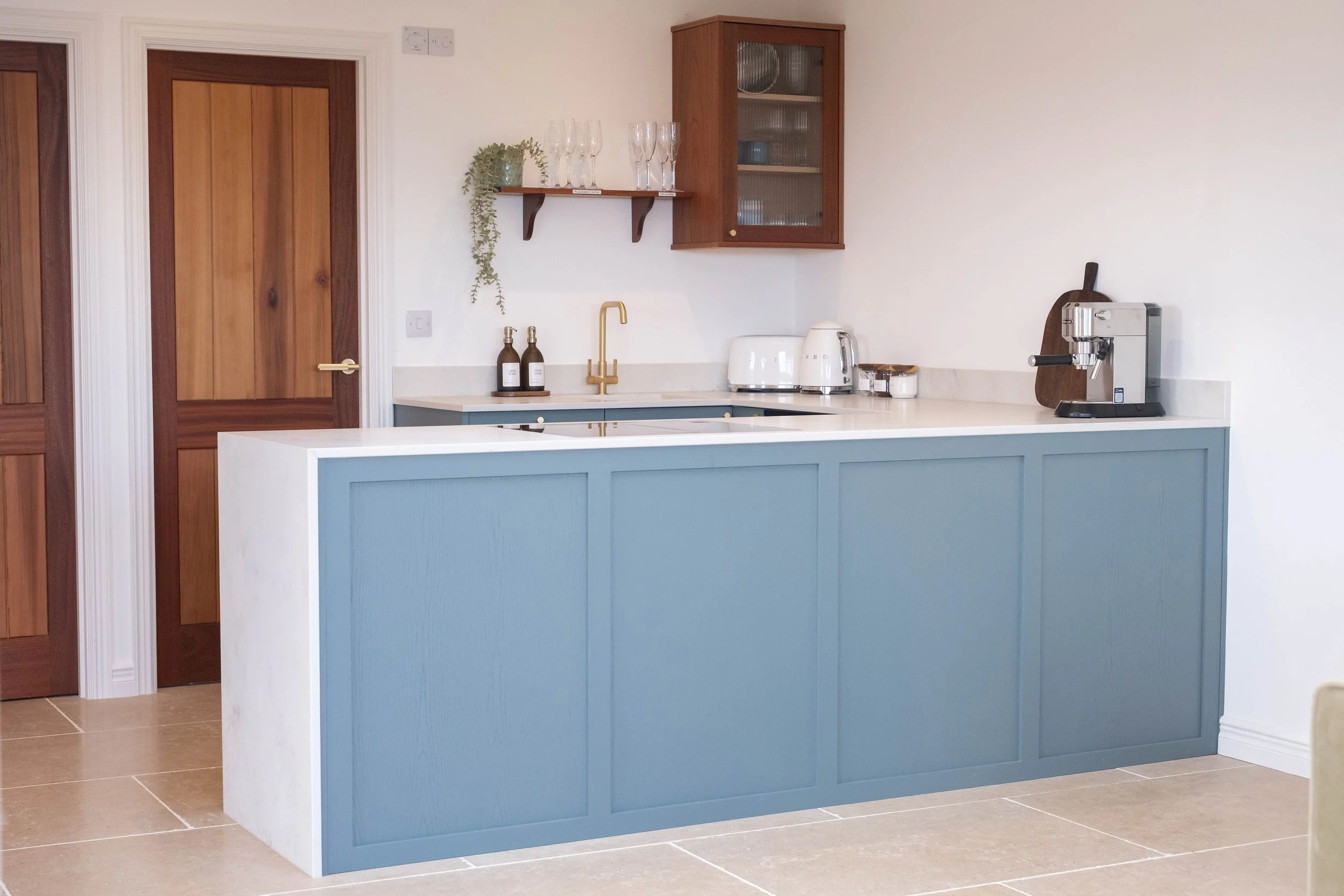 A kitchen with a blue island, white countertop, wooden cabinets, and various appliances including a toaster, coffee machine, and a small cutting board.
