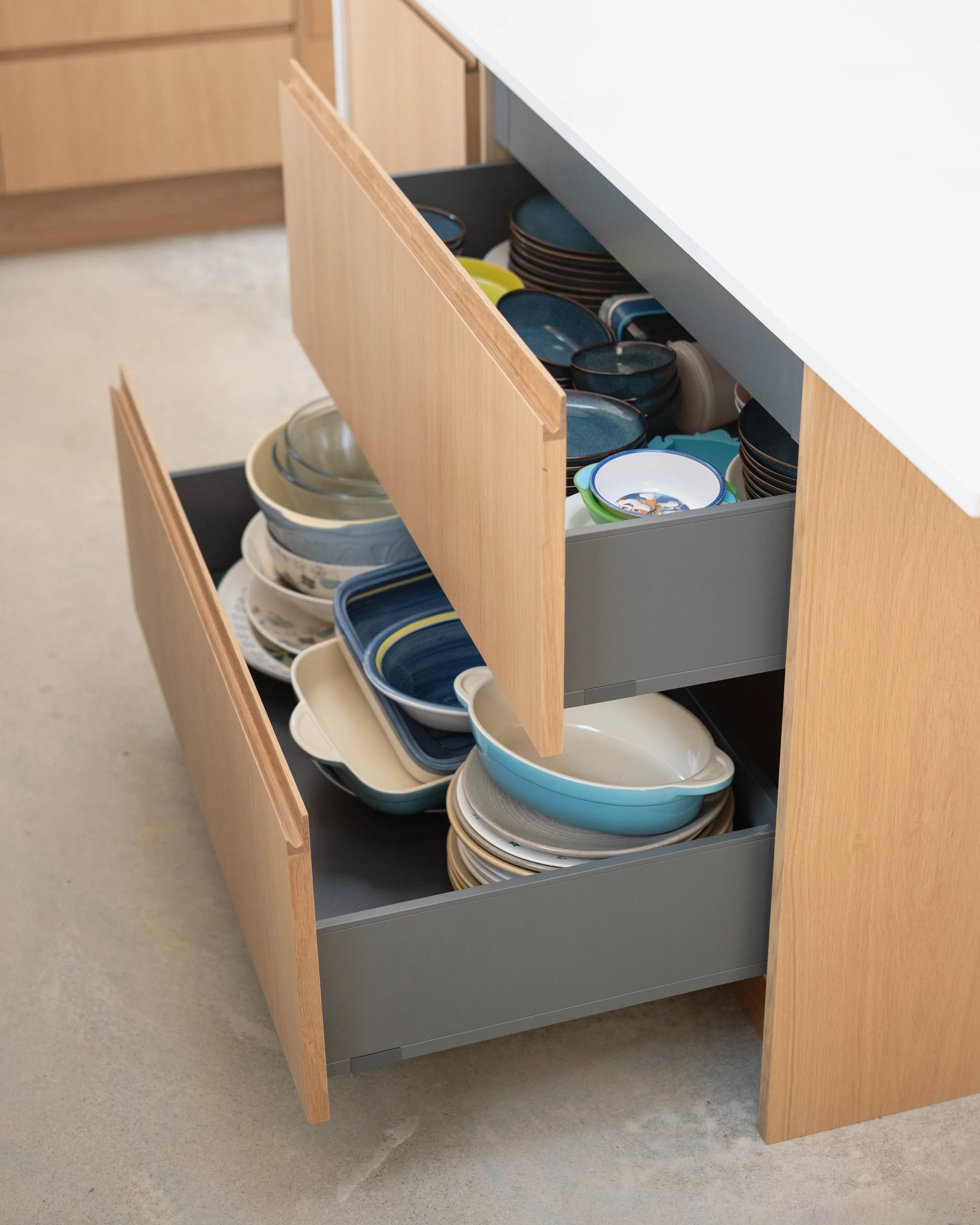 An open kitchen drawer filled with neatly stacked bowls of various sizes and colors, including blue, green, beige, and patterned designs.