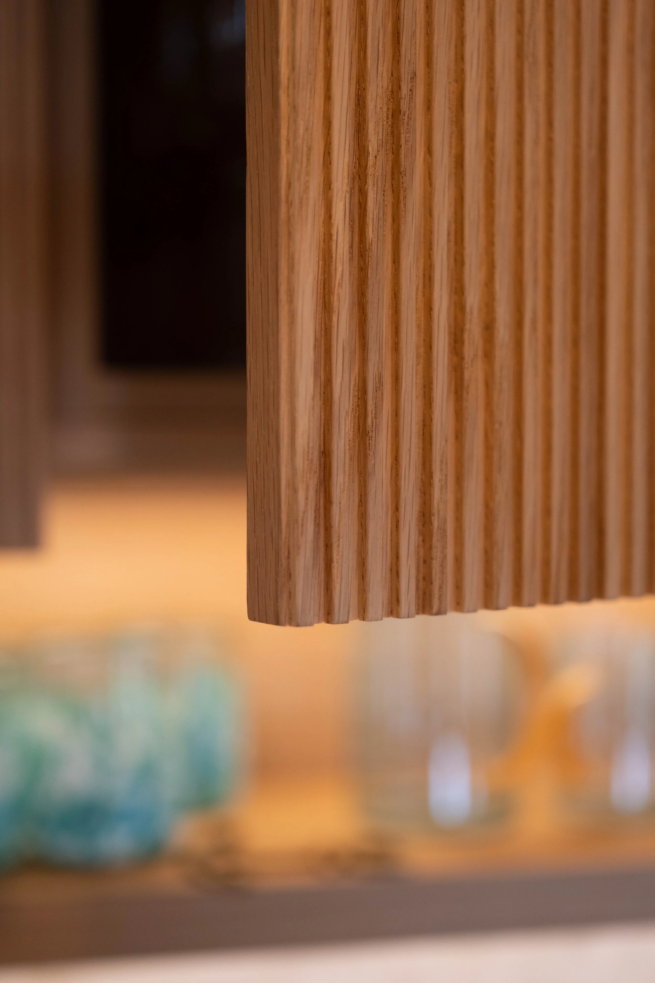 Close-up of a wooden furniture piece with vertical grooves, taken from underneath with blurred objects in foreground.