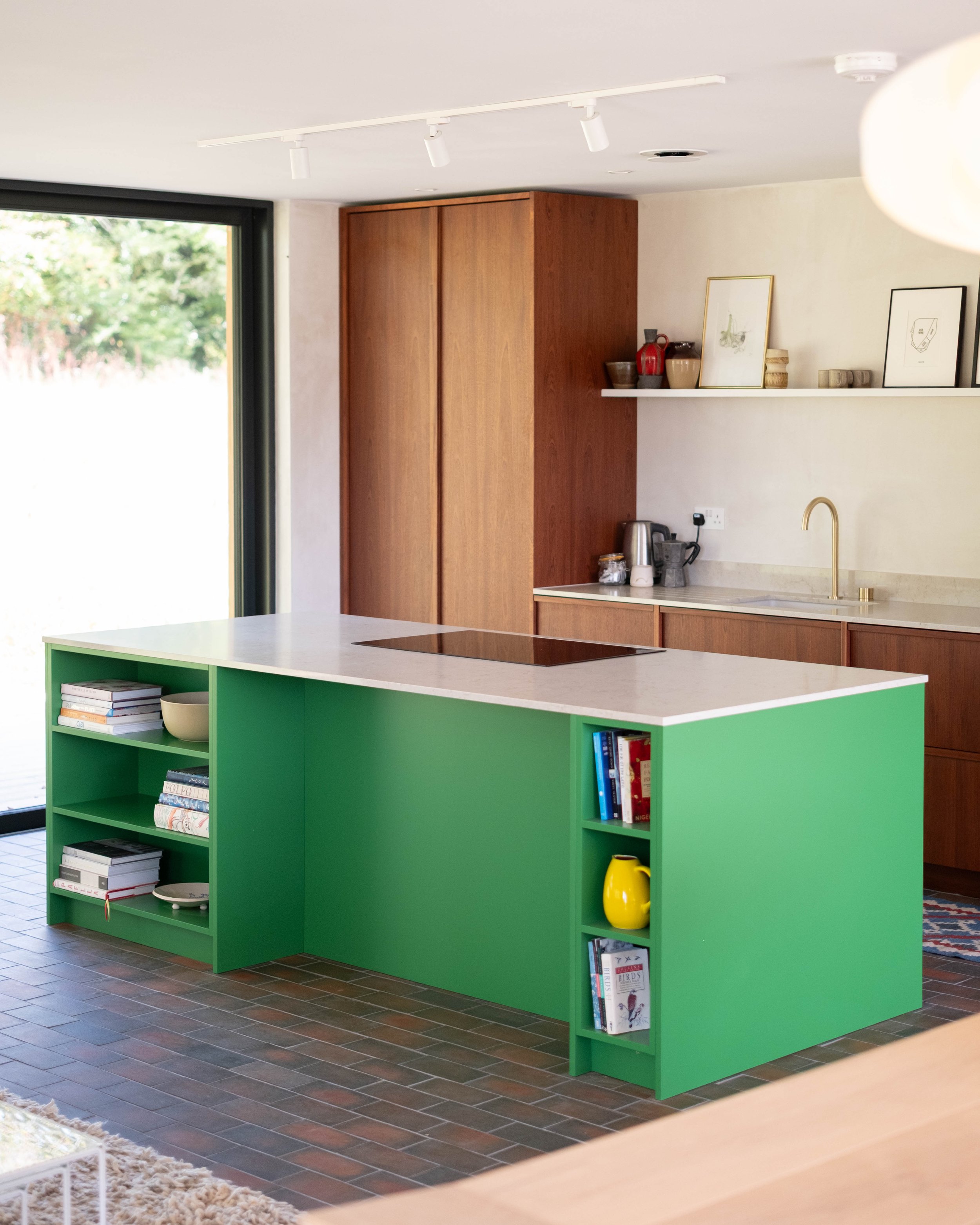 Modern kitchen with green open shelving, wooden cabinets, white countertops, and a large window with greenery outside.
