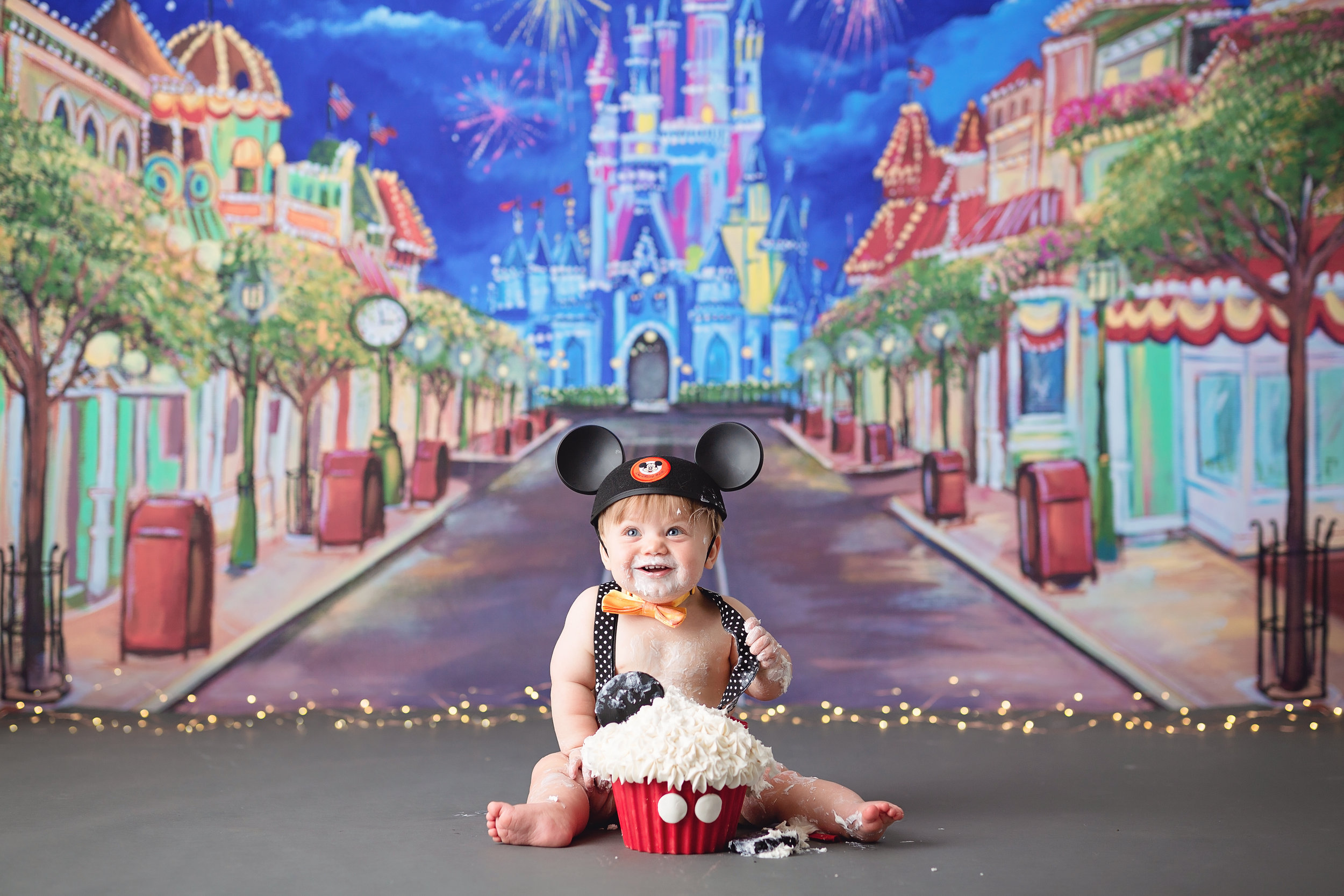  A Disneyland-themed cake smash featuring a backdrop of the Cinderella Castle from Magic Kingdom and cute baby wearing Mickey Mouse ears 