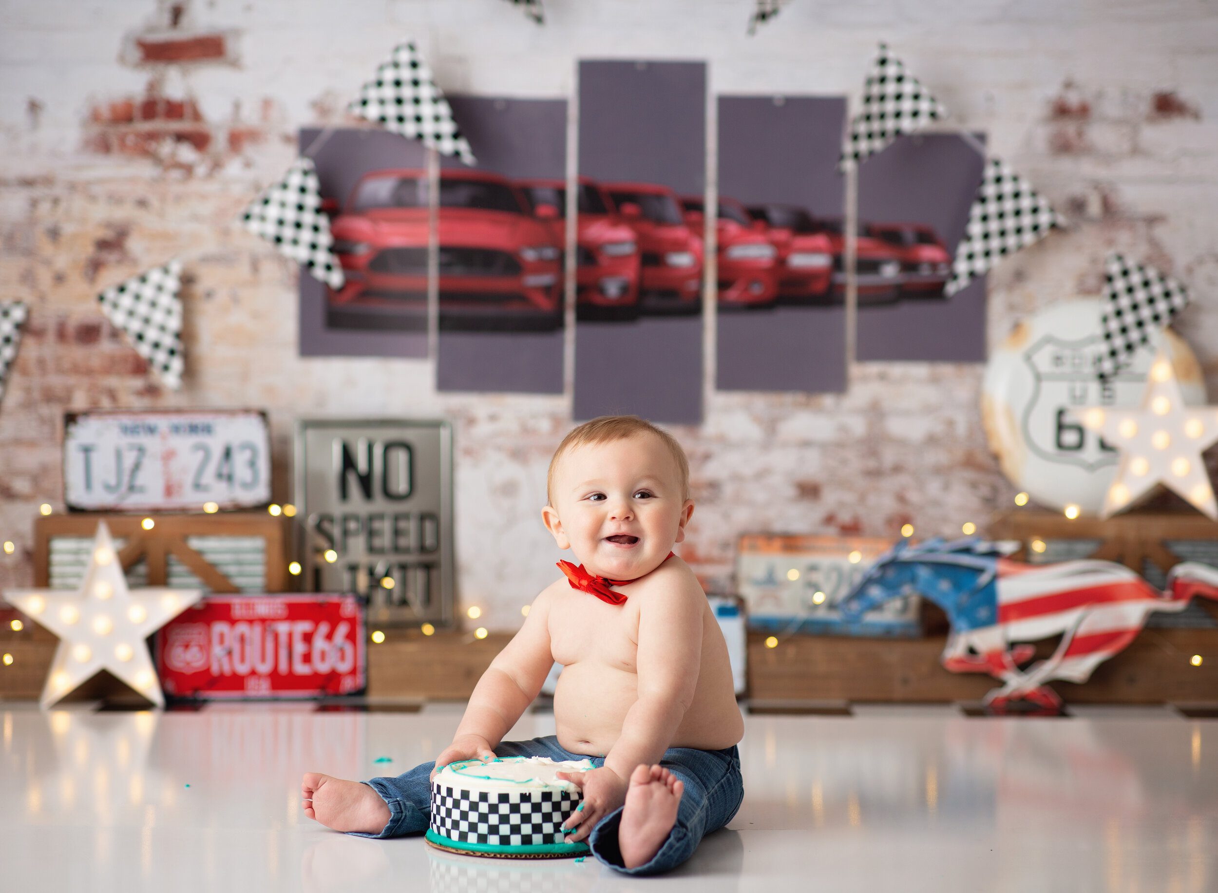 Chunky baby sitting on floor with a birthday cake against a customized race car backdrop 