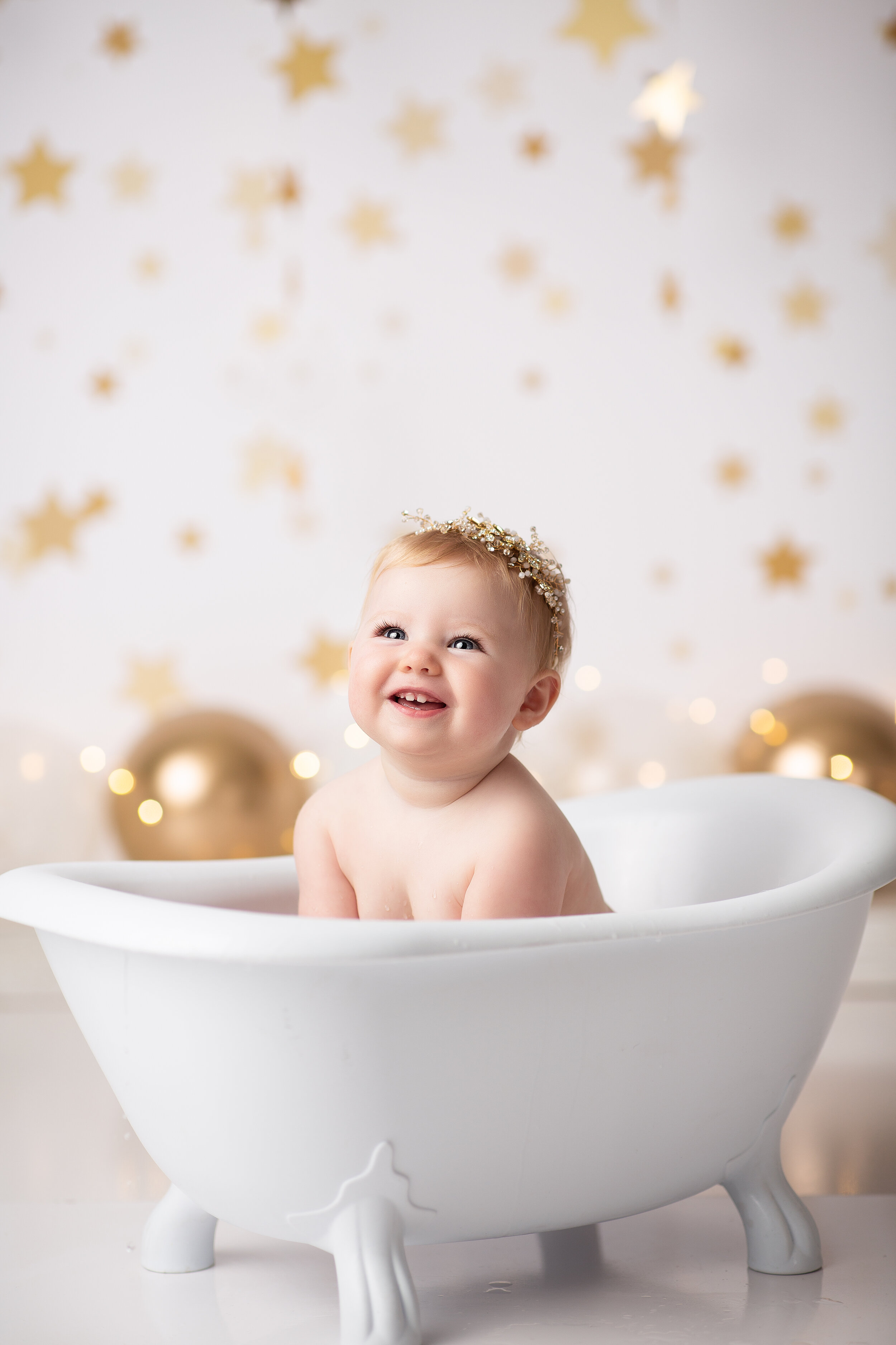  White and gold streamers decorate the studio while baby splashes below in the tub after her cake smash 