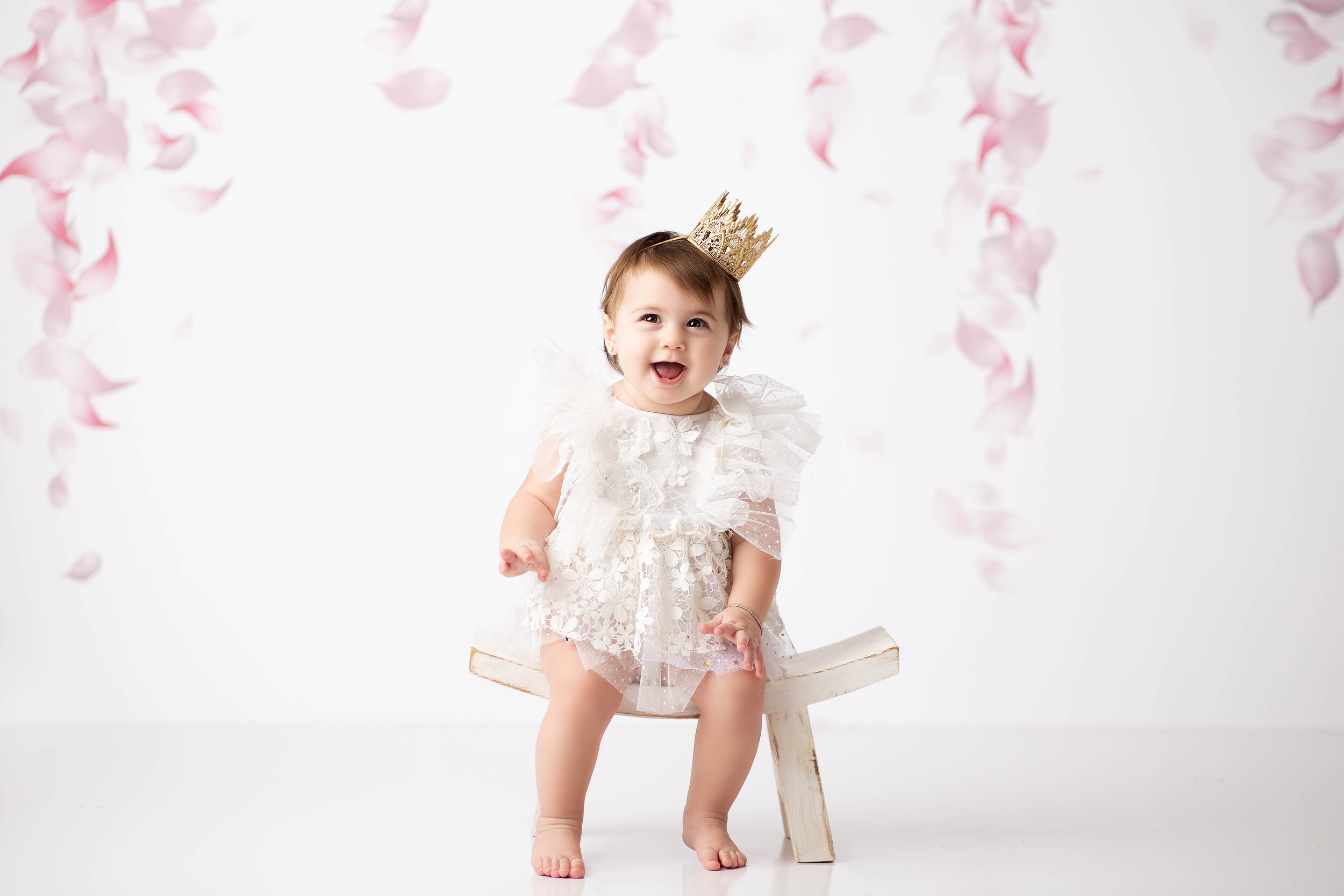  Young child laughing while seated on miniature bench during milestone photo session in studio 