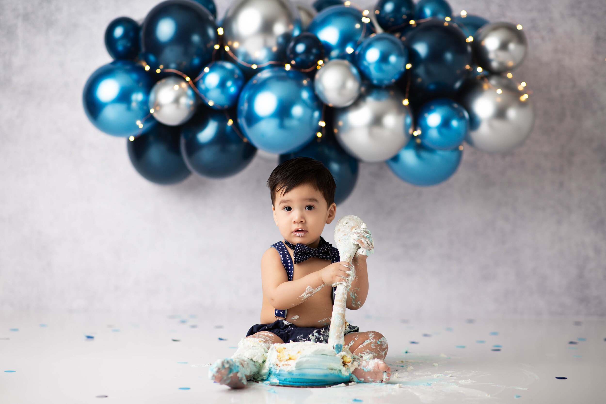  Asian baby covered in frosting and clutching wooden spoon after a birthday cake smash in New Jersey 