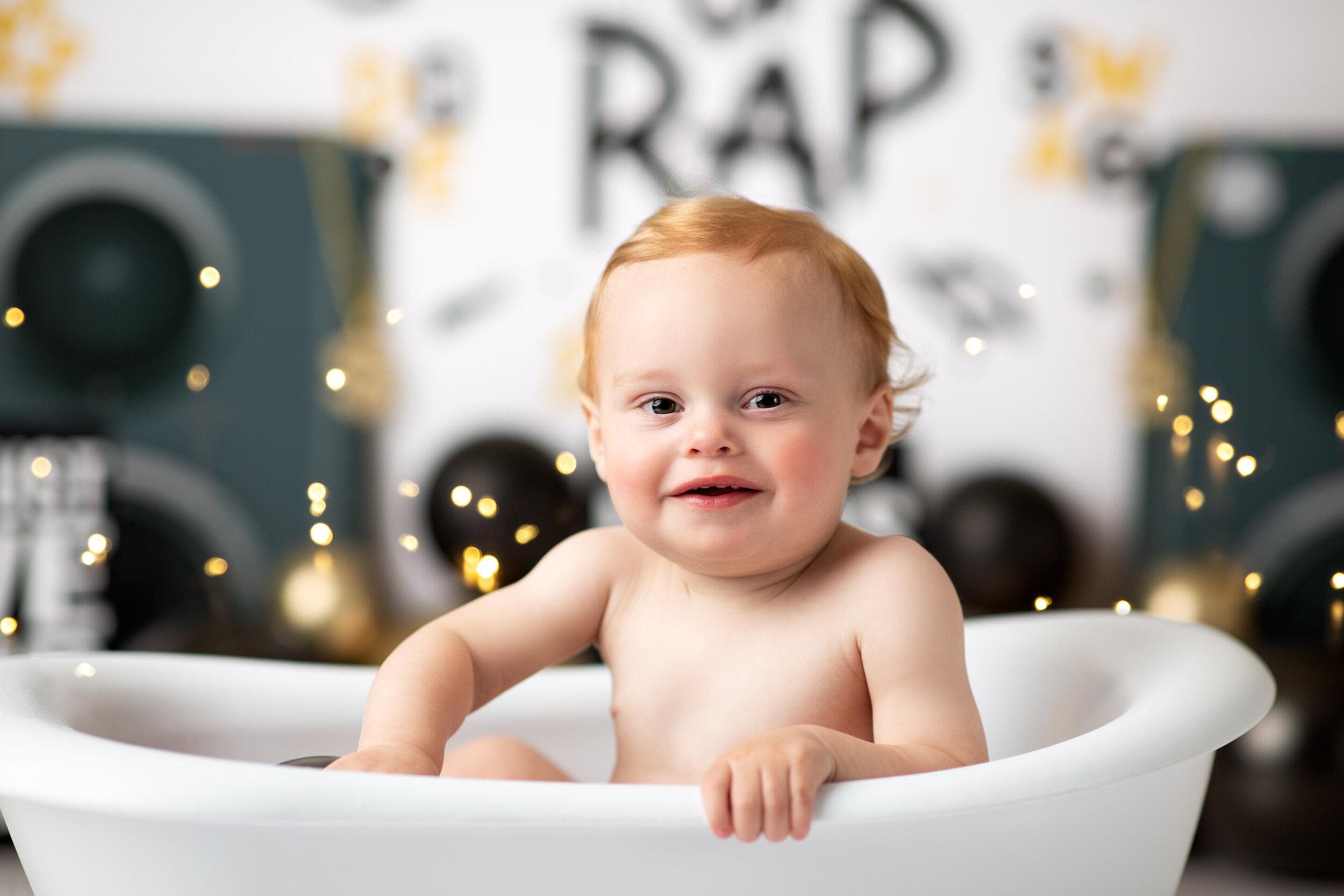  Redhaired baby grinning from a miniature bathtub after his King of Rap birthday cake smash 