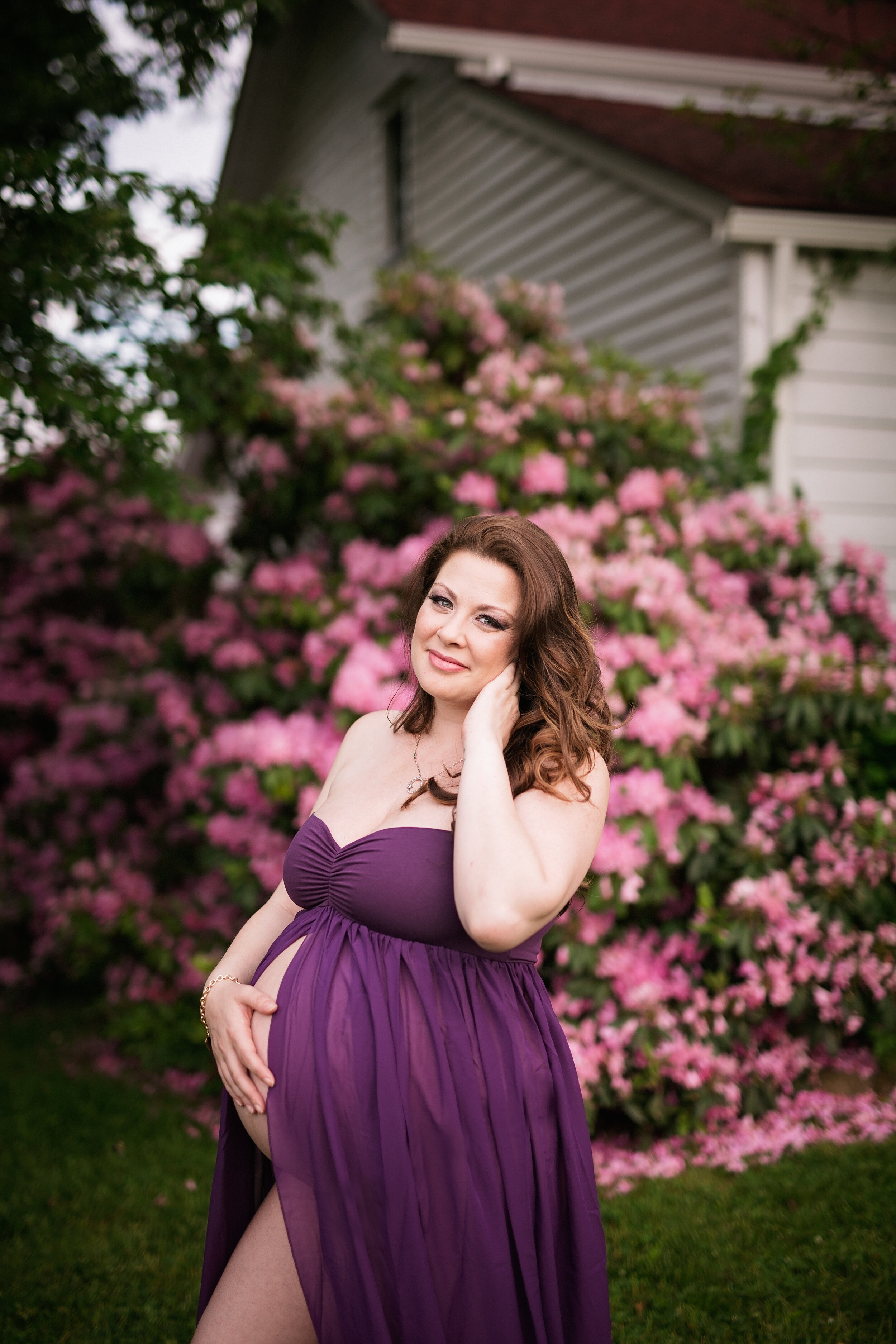  Woman in purple maternity gown posing in front of flowerbed 