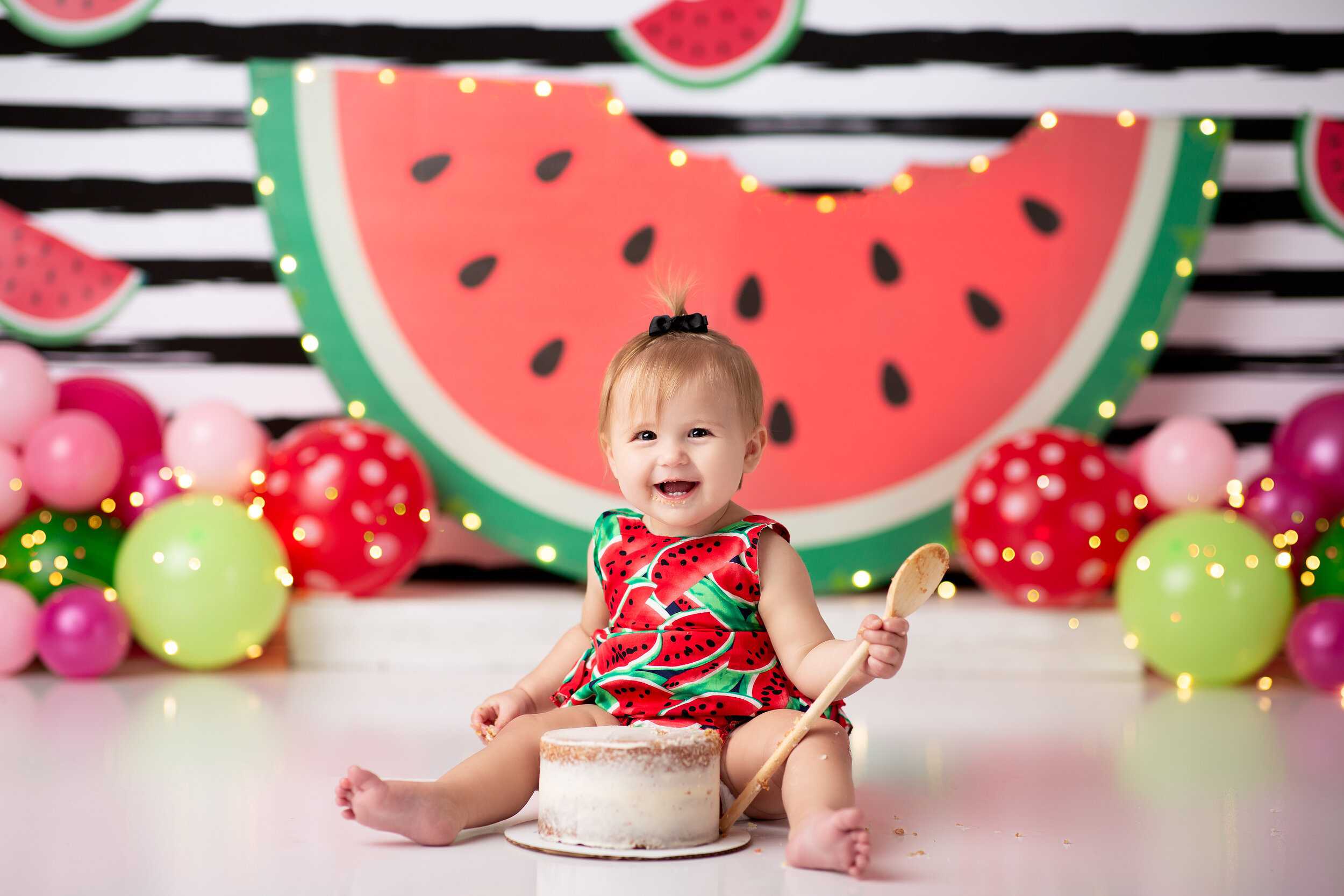  Laughing baby girl dives into her cake with a spoon during a watermelon themed cake smash in North Jersey 