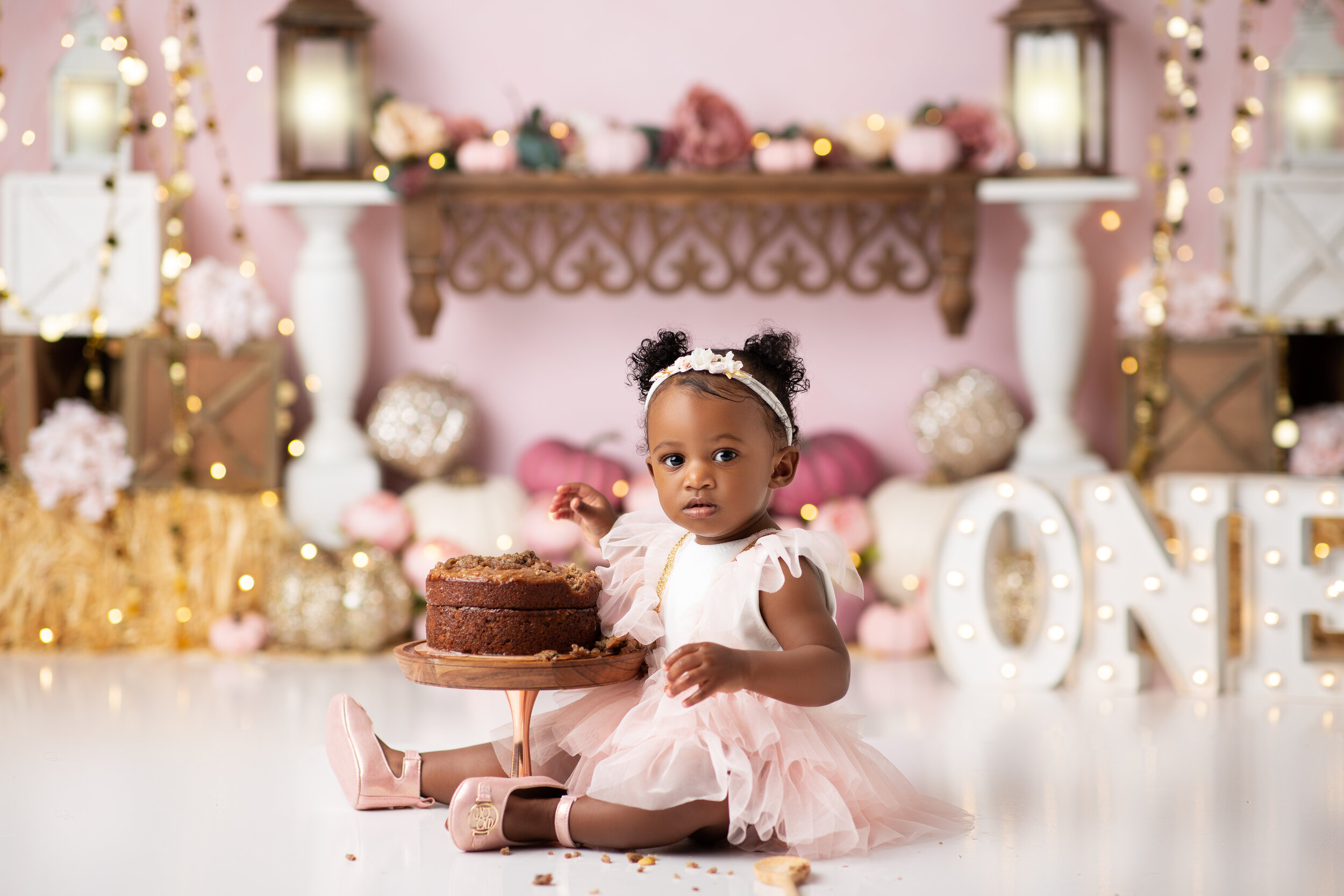  African American baby girl prepares to eat her birthday cake during a pink and gold pumpkin themed cake smash 