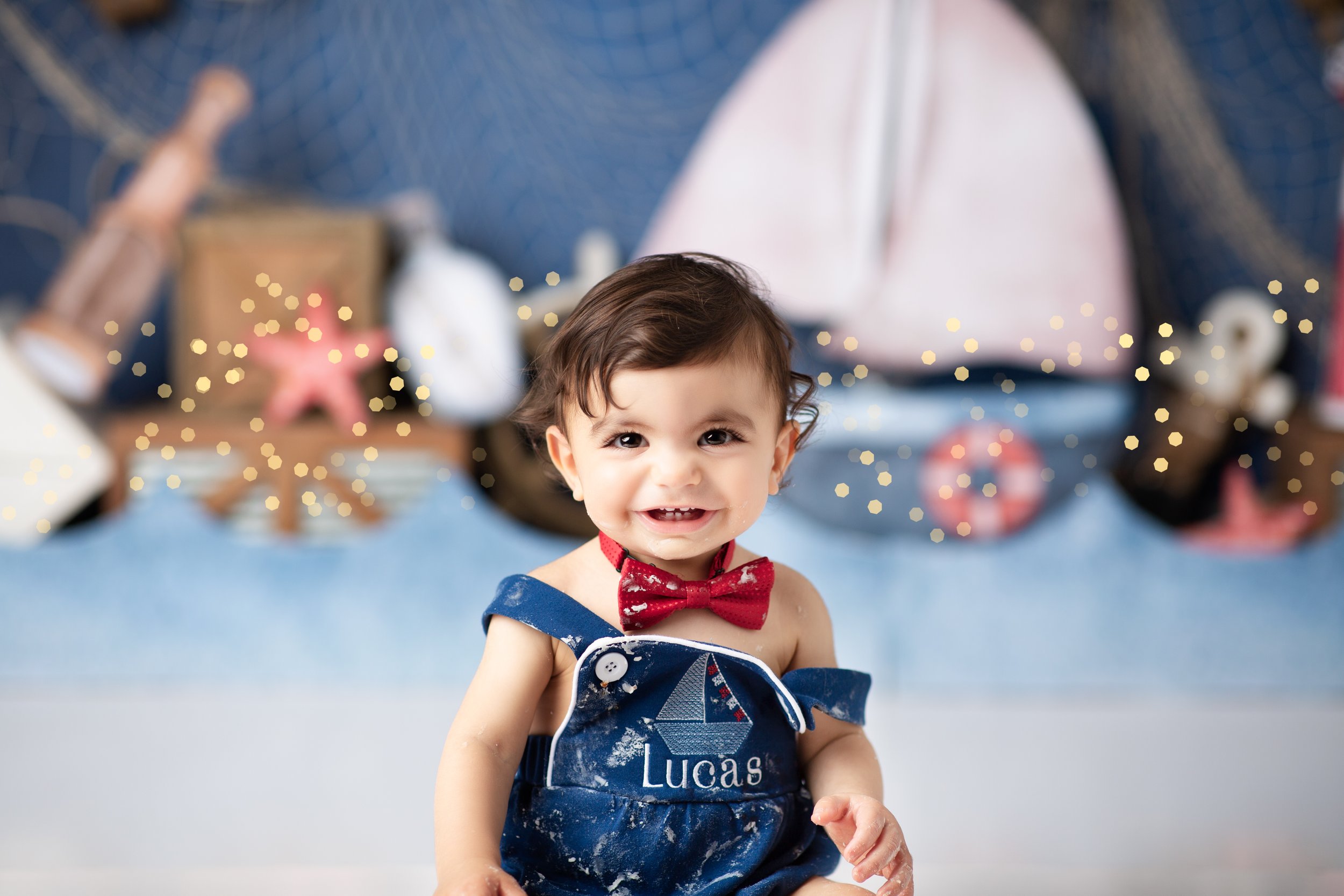  Smiling boy in blue overalls and red bow tie with a nautical scene behind him 