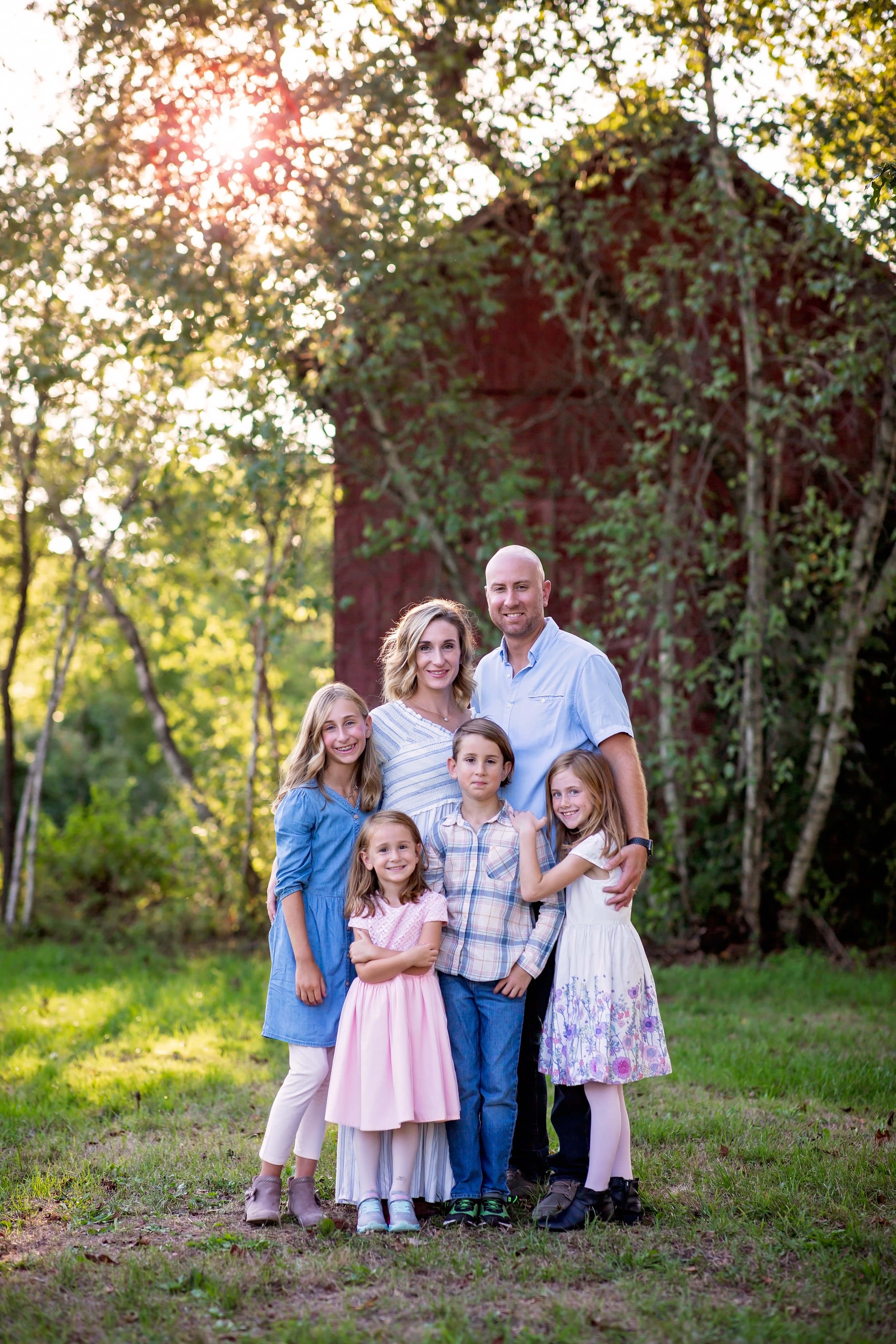  Family poses in front of red barn and trees 