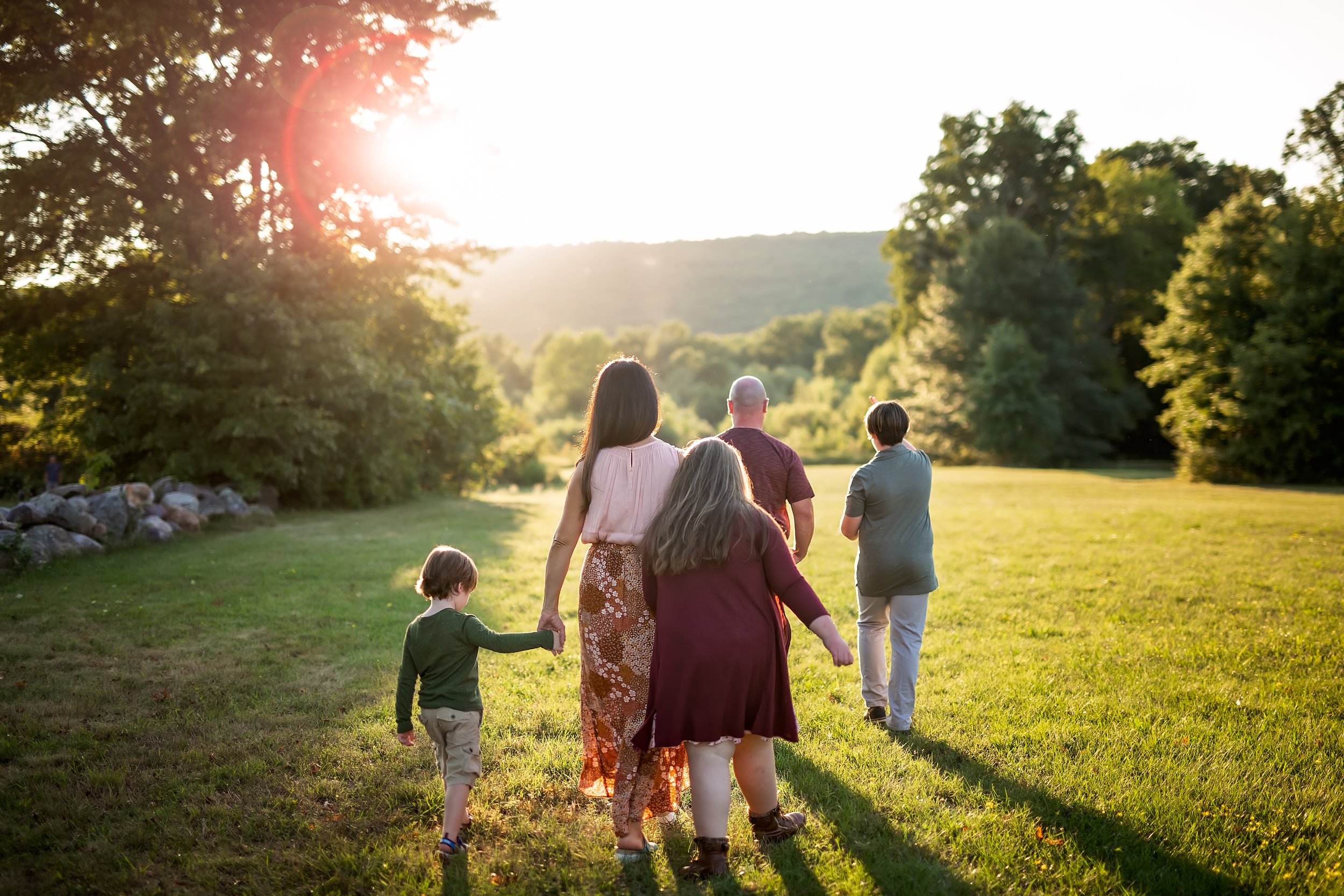  Back view of family holding hands as the walk together towards the sunset and the hills 