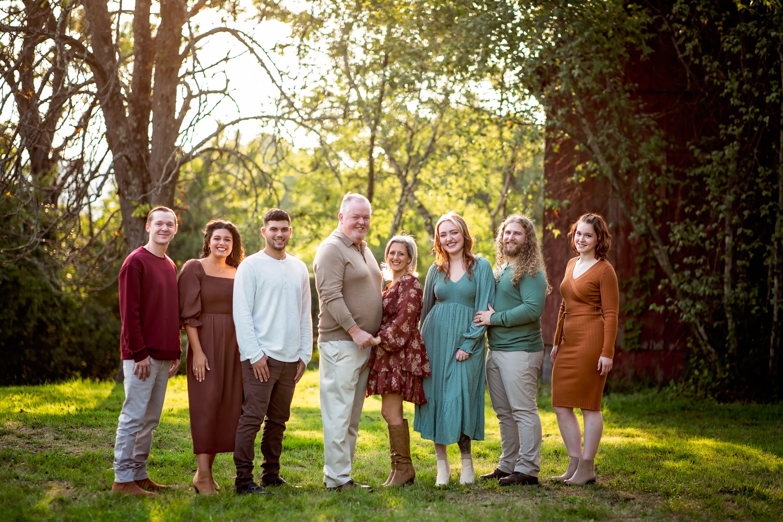  Parents with their grown and married children stand together for a family portrait in a wooded NJ park 