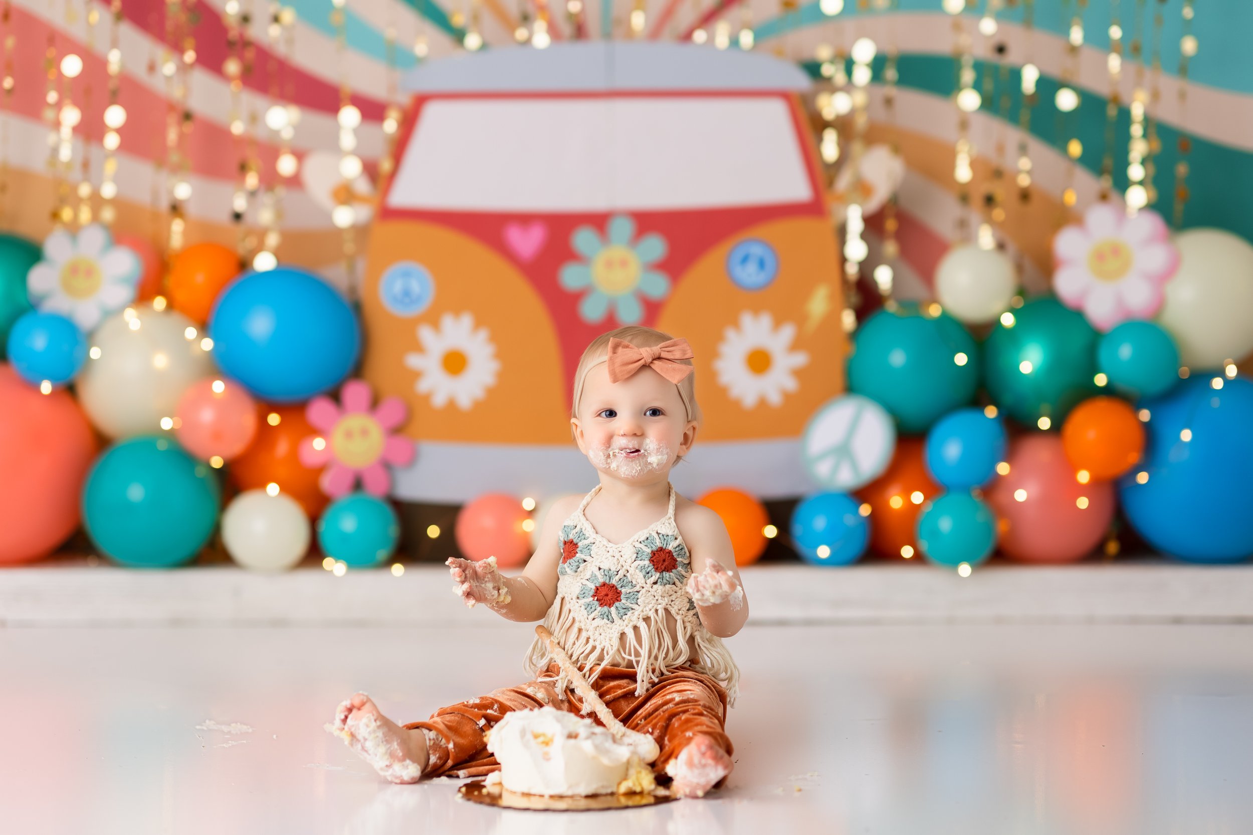  Free spirit baby dives into her cake with colorful balloons and a VW van cutout in the background 