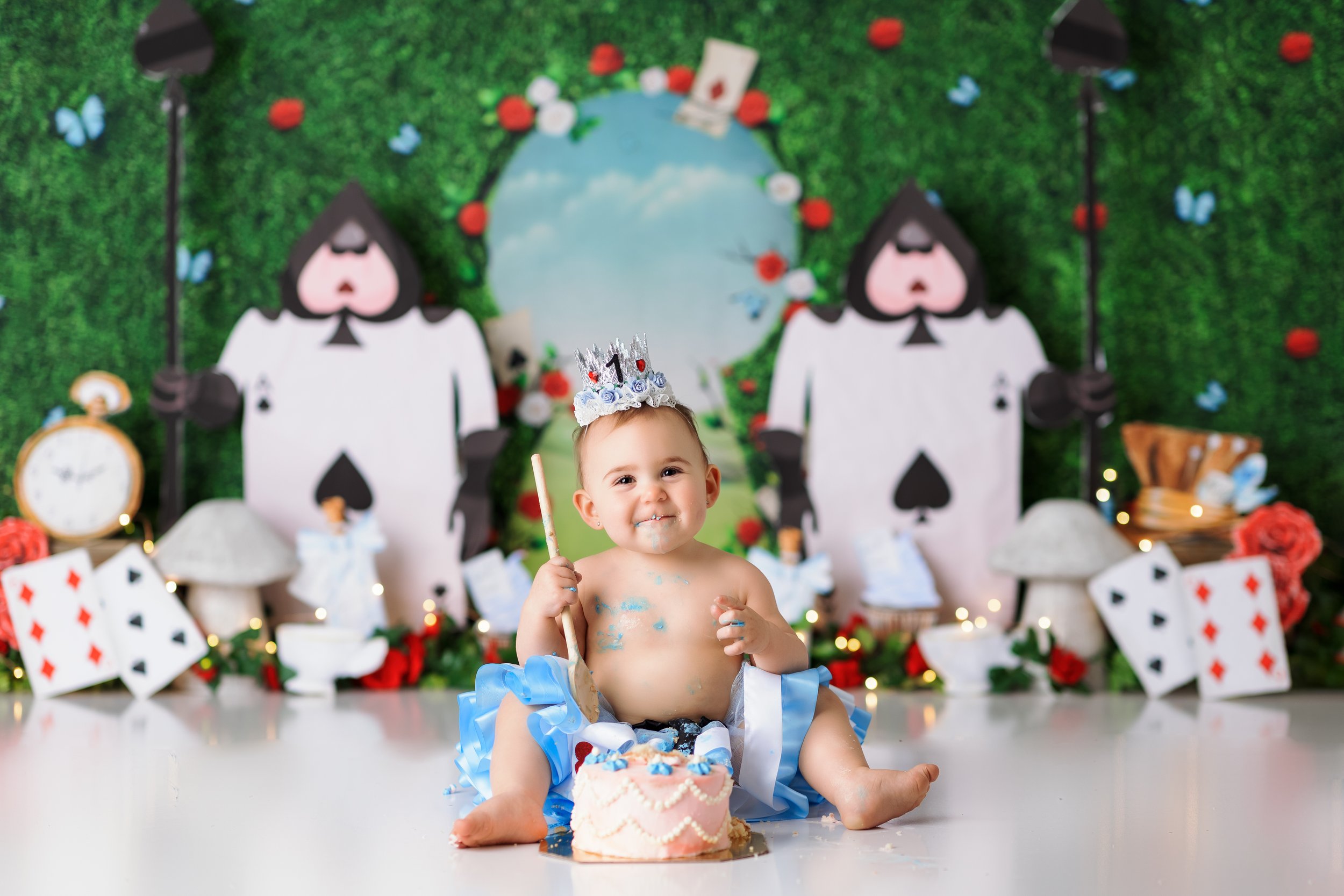  Baby girl in blue dress digging into her cake during an Alice in Wonderland custom cake smash session in New Jersey 