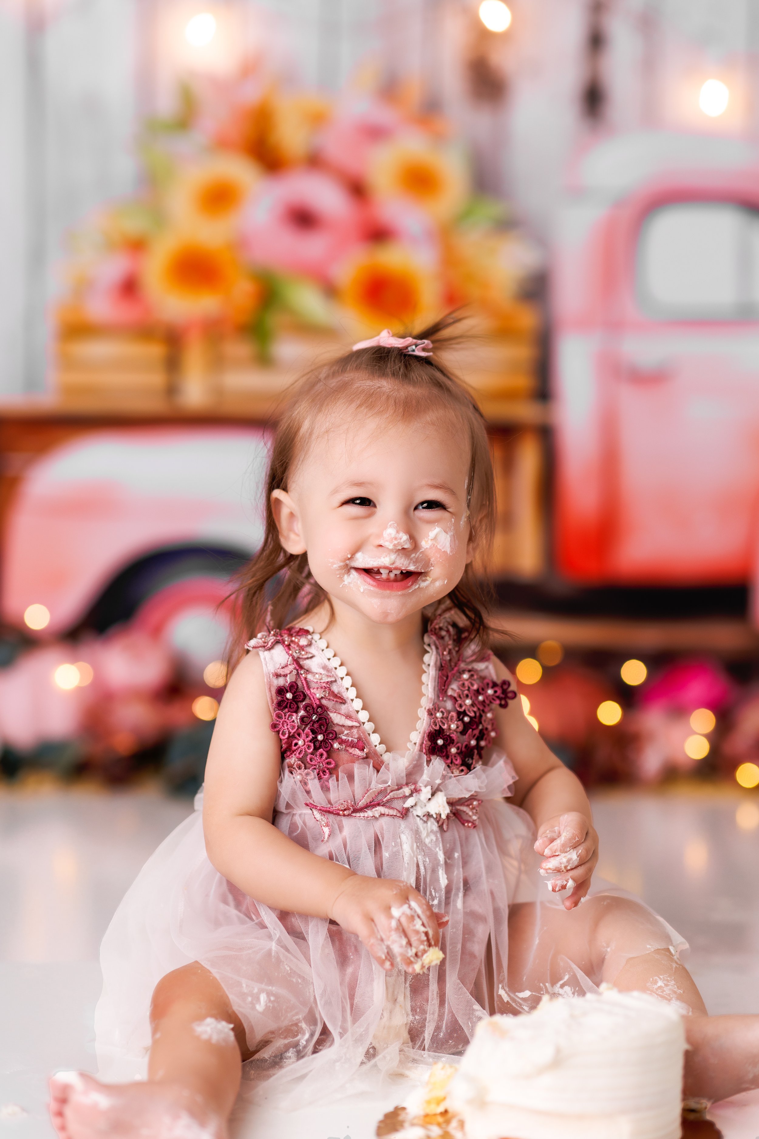  Toddler girl with icing all over her face smiles as she enjoys her custom cake smash in New Jersey 