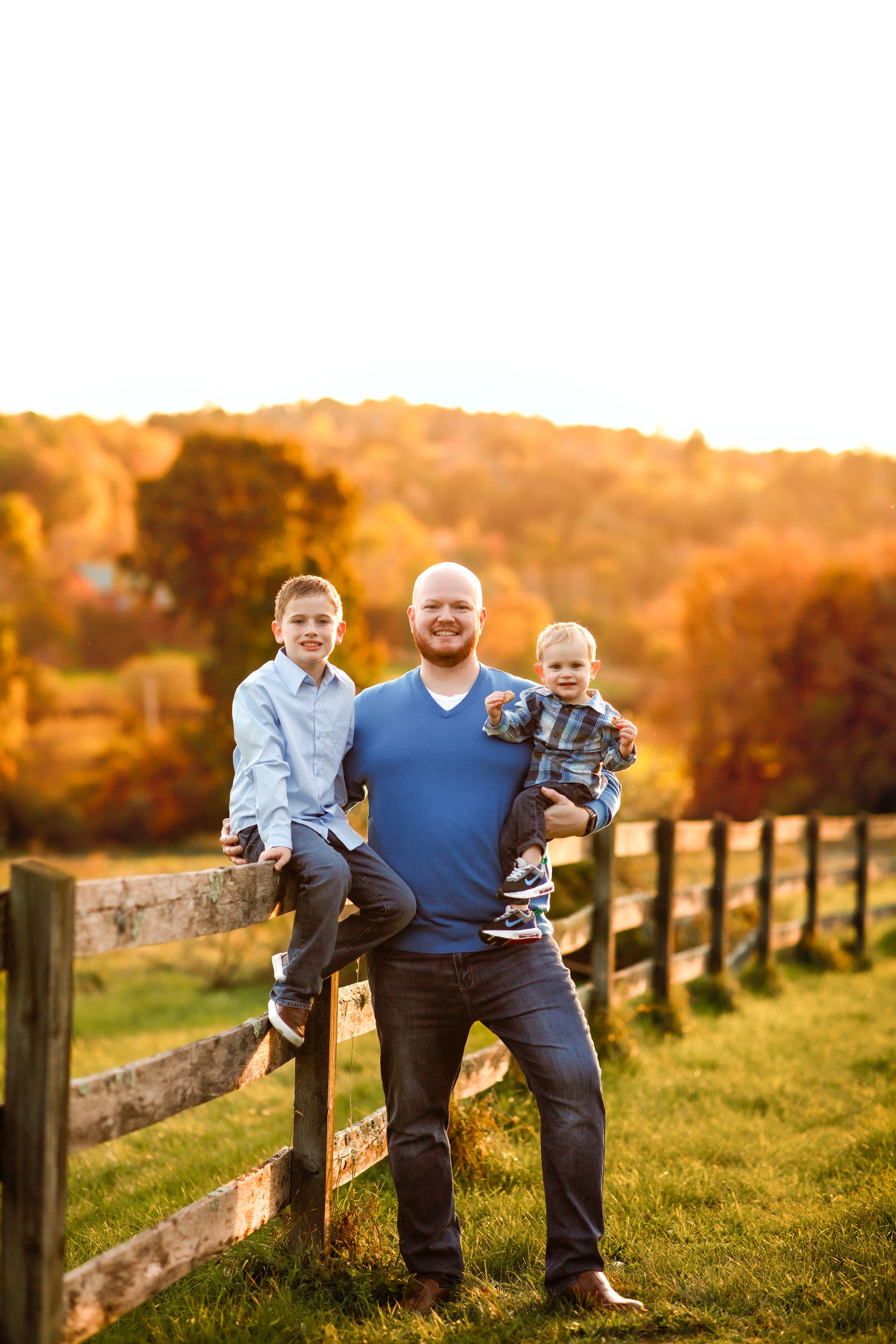  Dad and his two young sons pose near a rustic wooden fence in New Jersey with a backdrop of fall foliage 