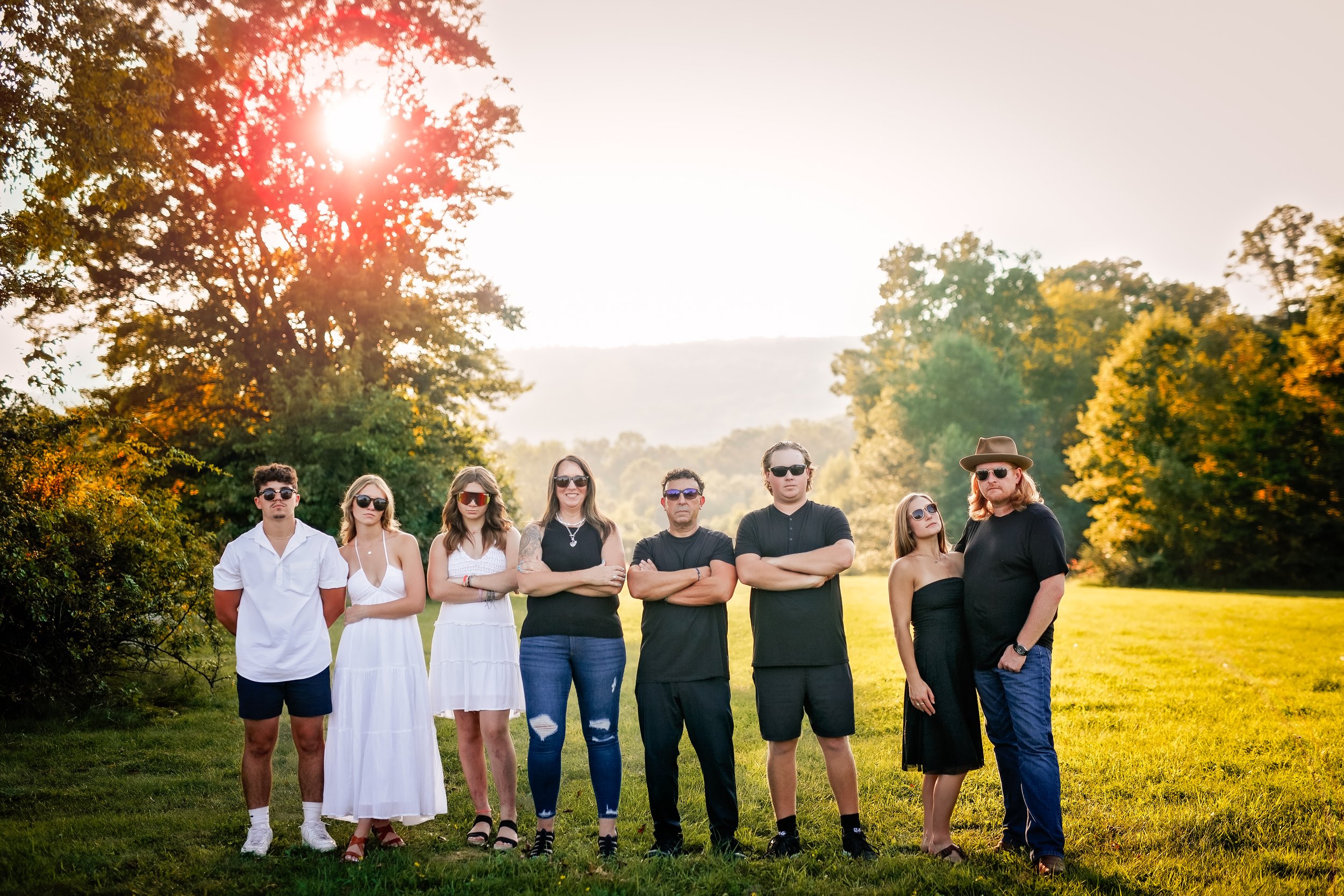  Family in sunglasses stand in a row with their arms folded, striking a pose for a comedic shot during their family photo session 