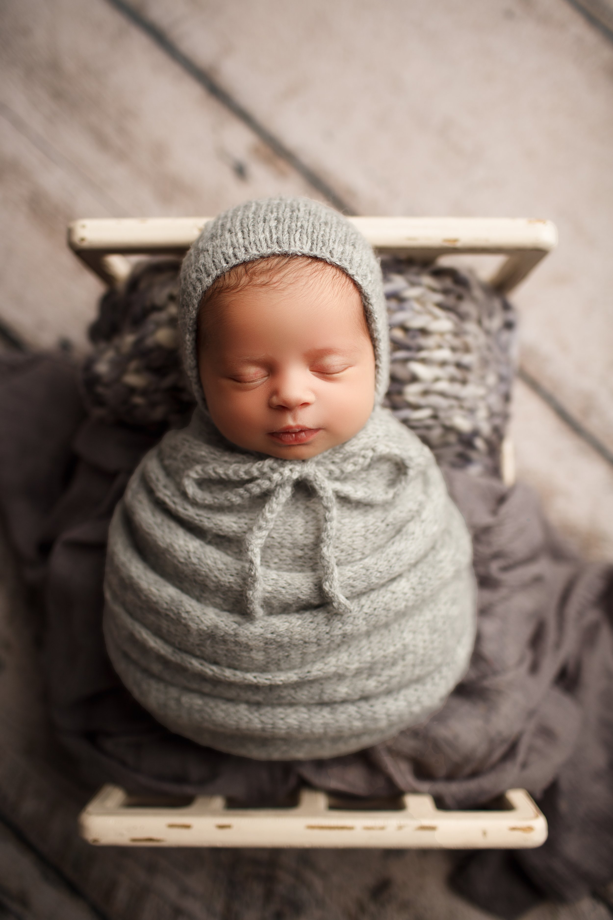  Baby in gray swaddle and hat asleep in miniature wooden crib 