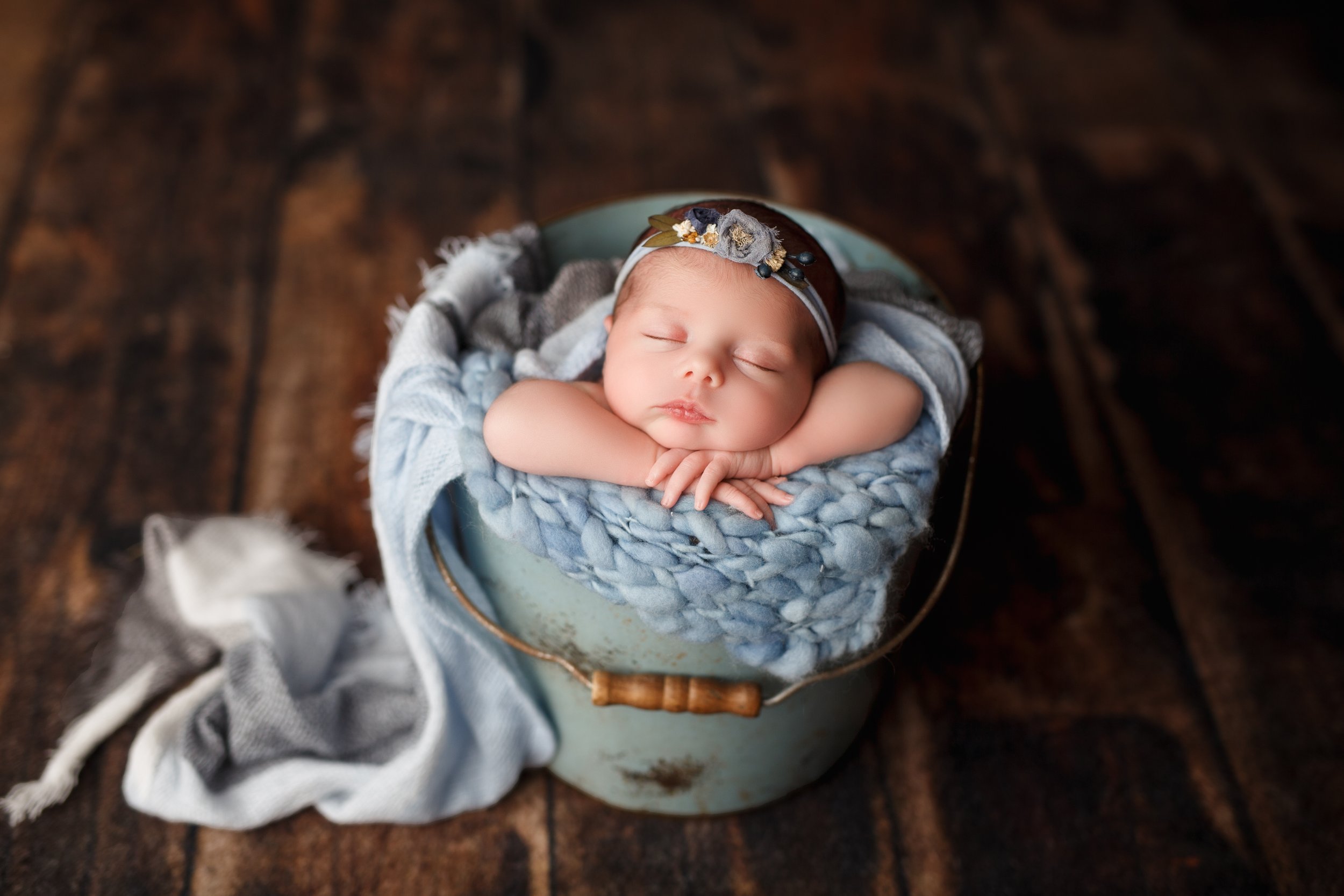  Baby girl in cozy blue wrap sleeps with her chin on her hands in an old-fashioned bucket 