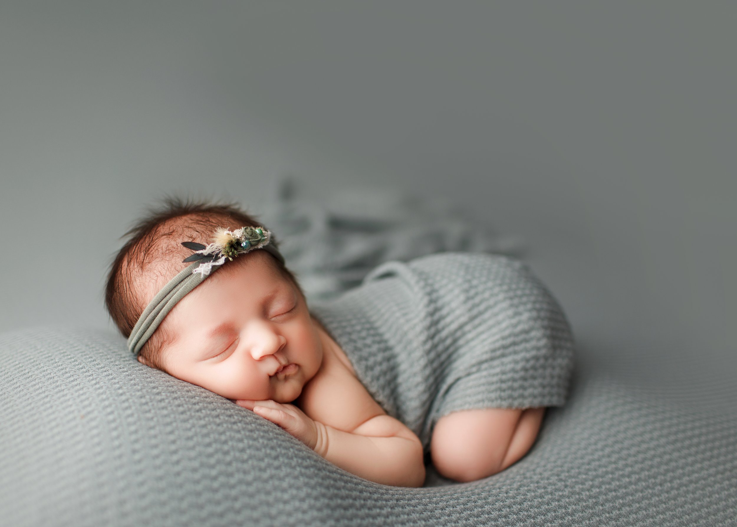  Baby girl asleep on tummy on soft gray beanbag wearing a gray wrap and headband 