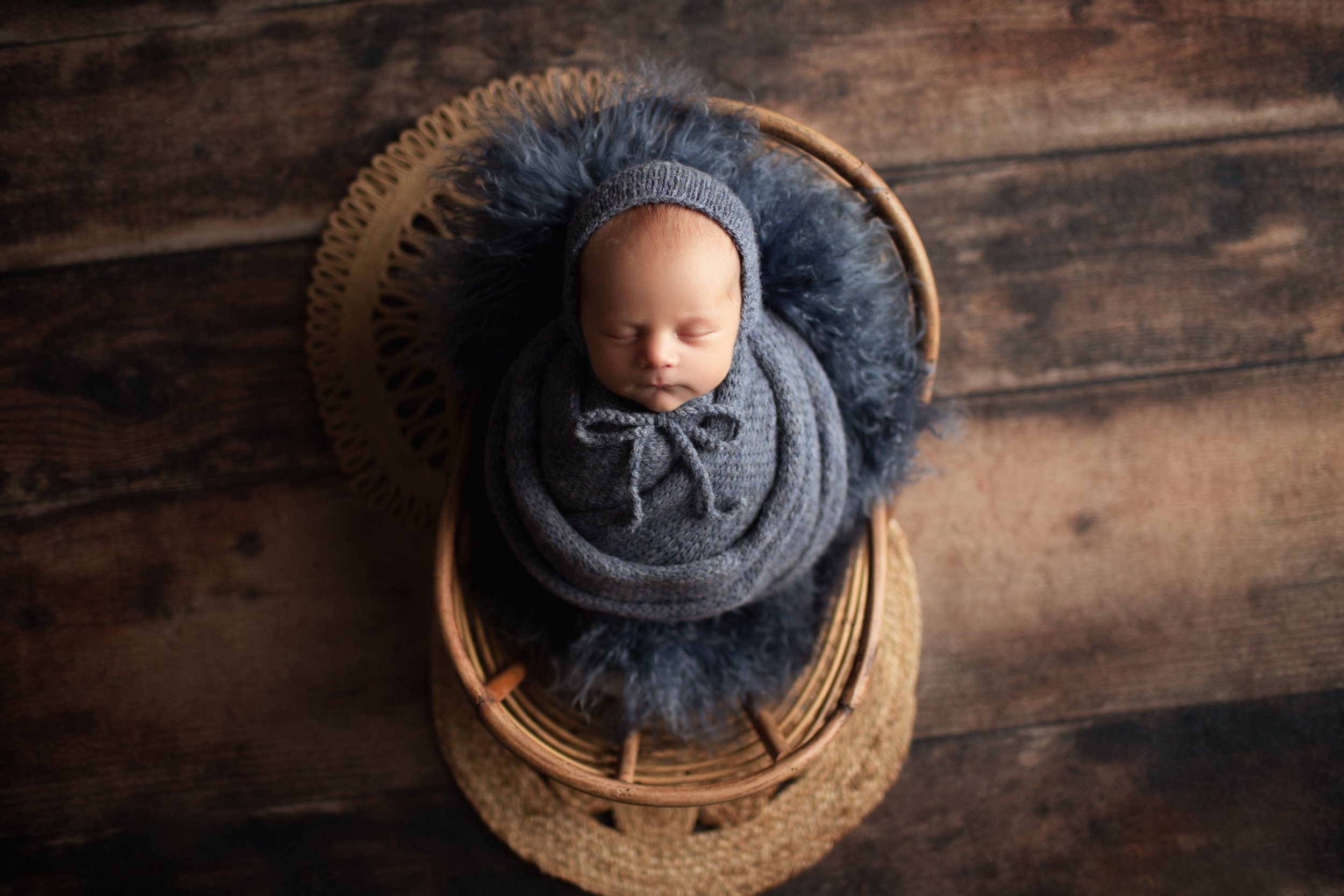  Baby boy in blue swaddle asleep in wicker prop chair in New Jersey studio 