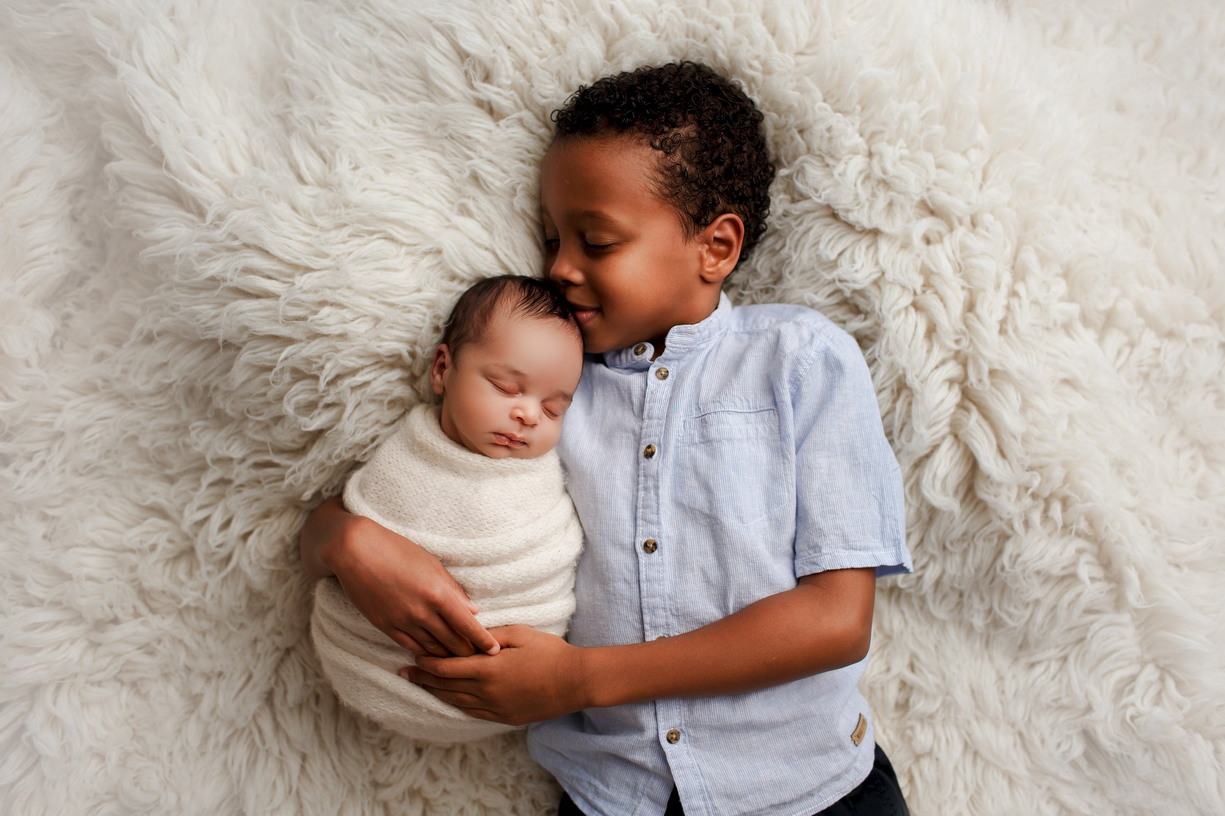  Young boy wraps his arms around his new baby brother and kisses the top of the little one’s head 