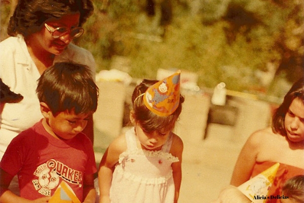 Alicia, 3, blows out the candles of a cake that her mom (standing behind her) made.