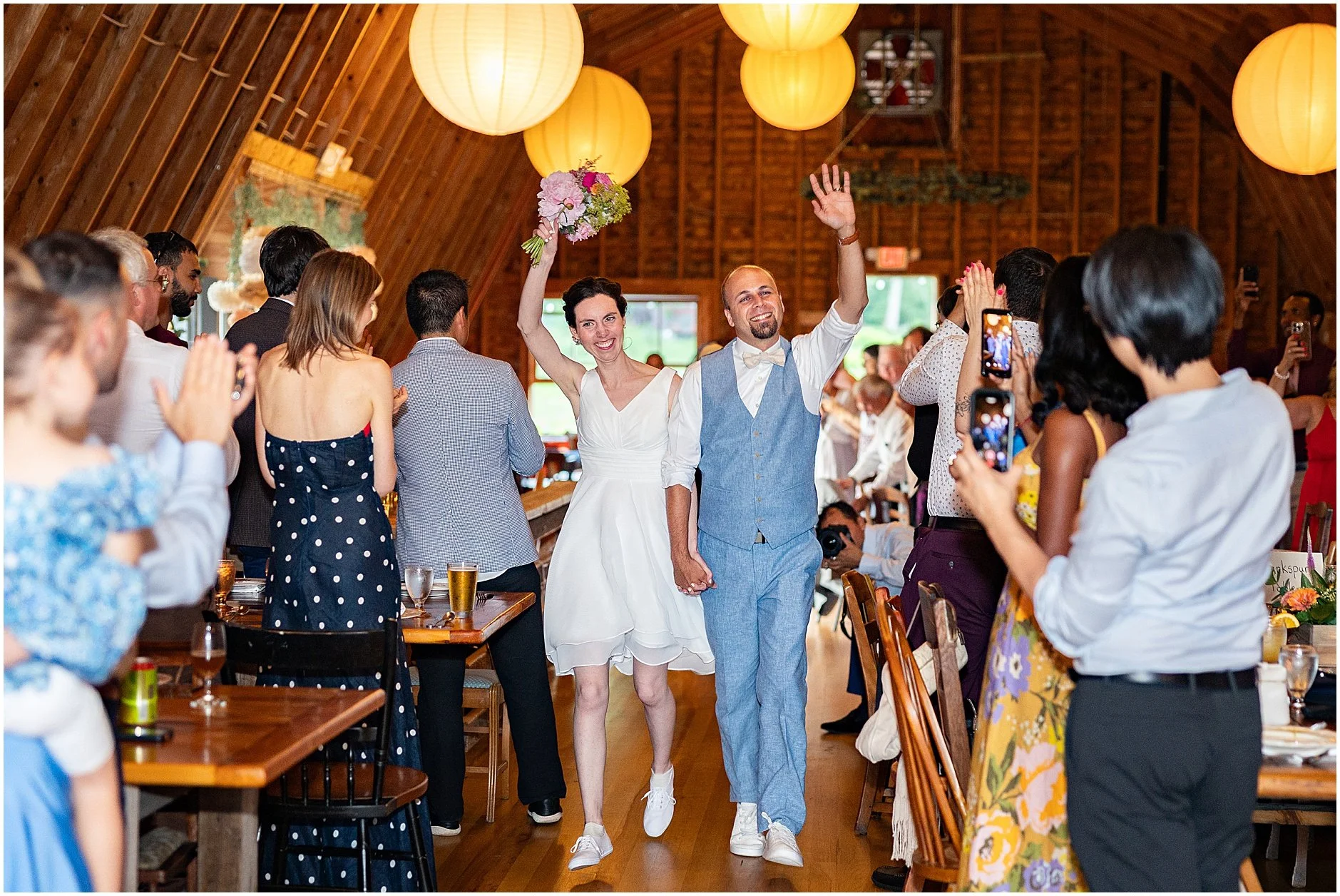 Newlyweds smiling and waving as they enter their reception surrounded by loved ones