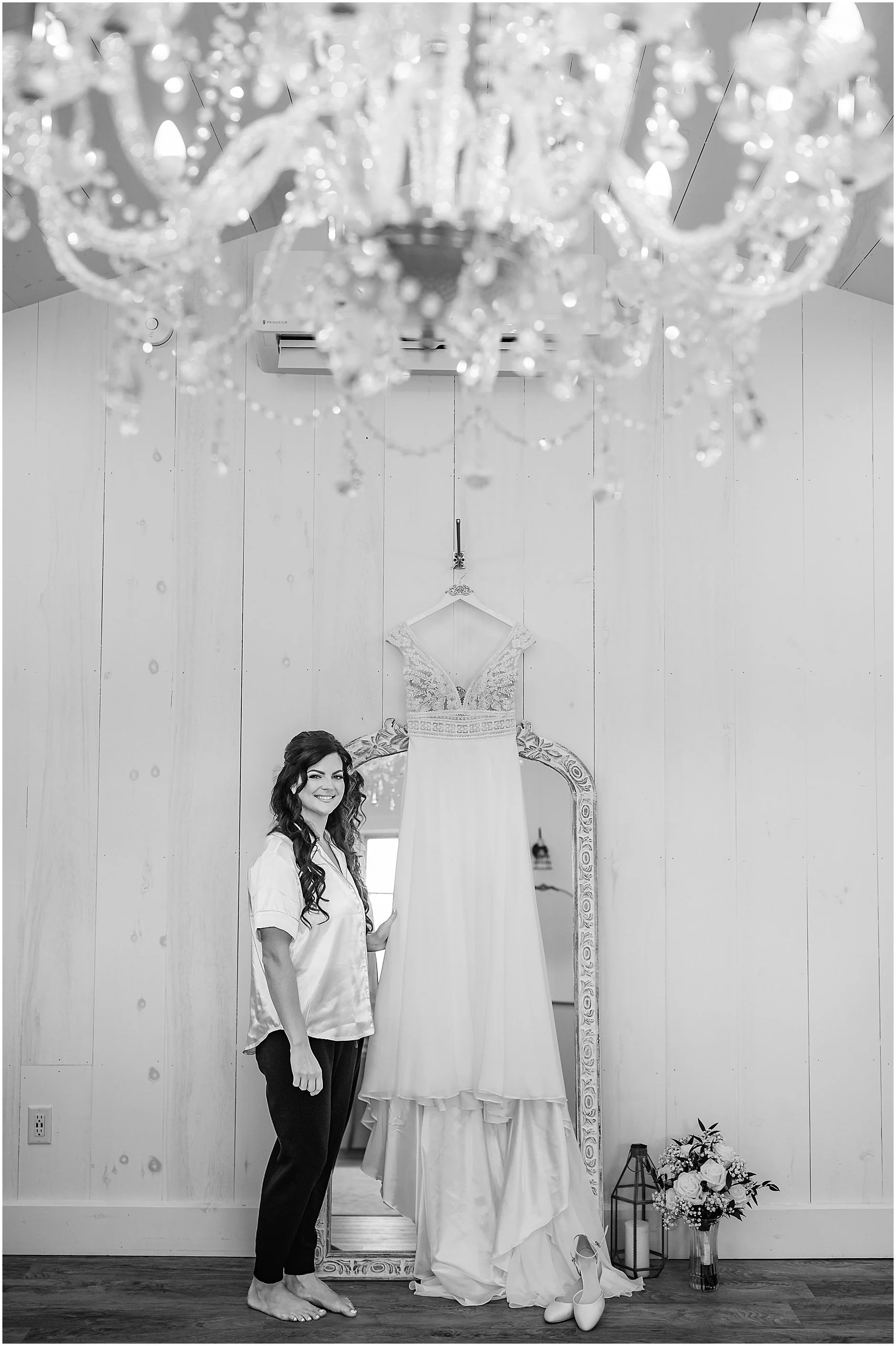 Black and white photo of bride standing with her dress hanging before putting it on