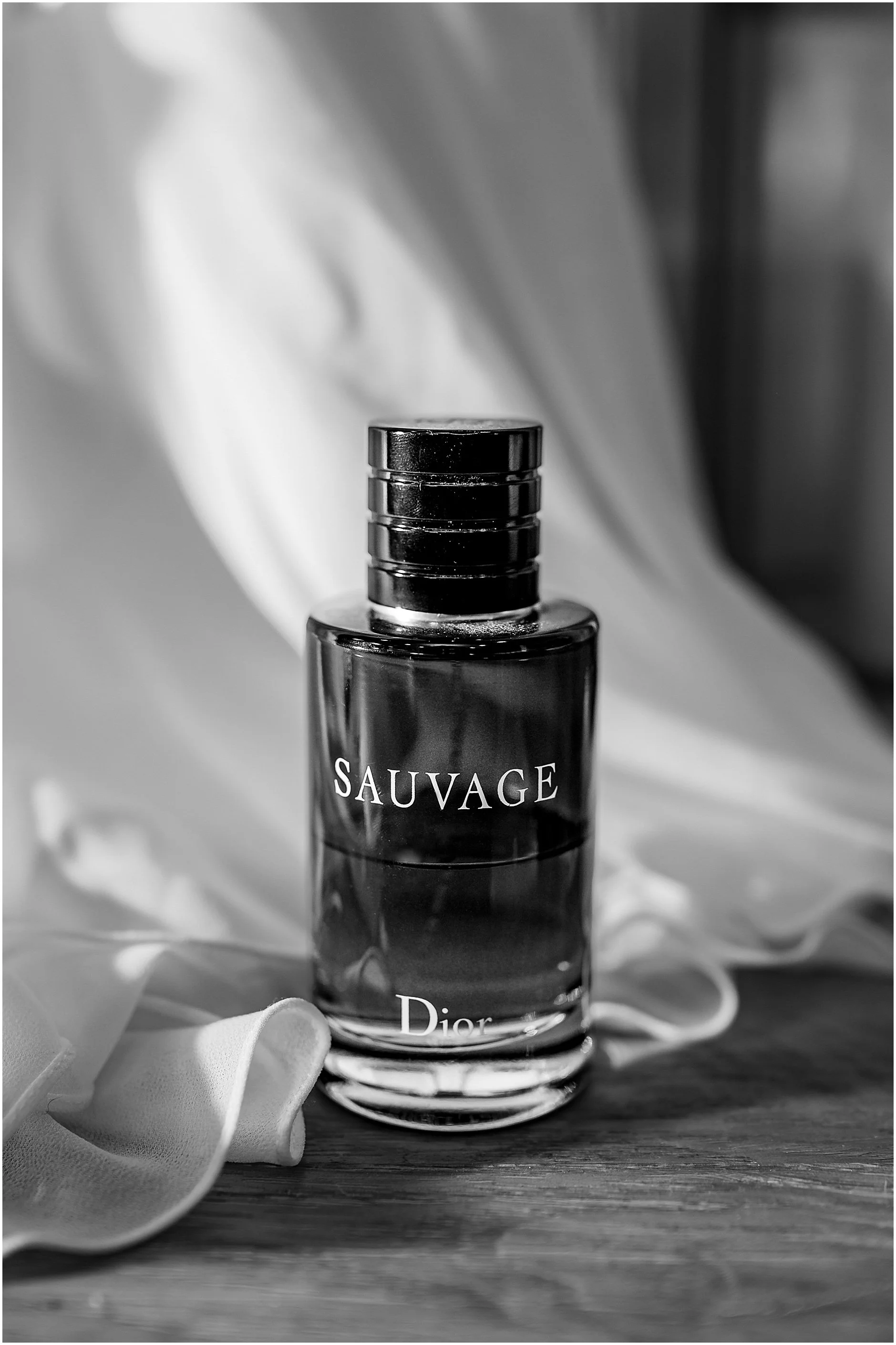Black and white image of Dior sauvage perfume against bride's wedding dress