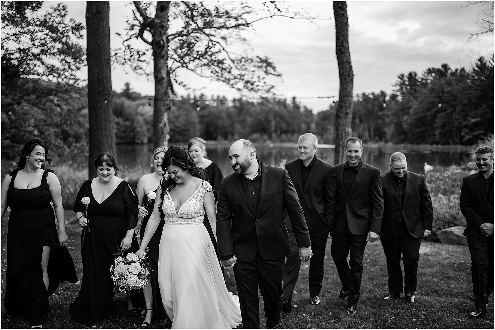 Black and white image of bride and groom laughing together with their wedding party by their side