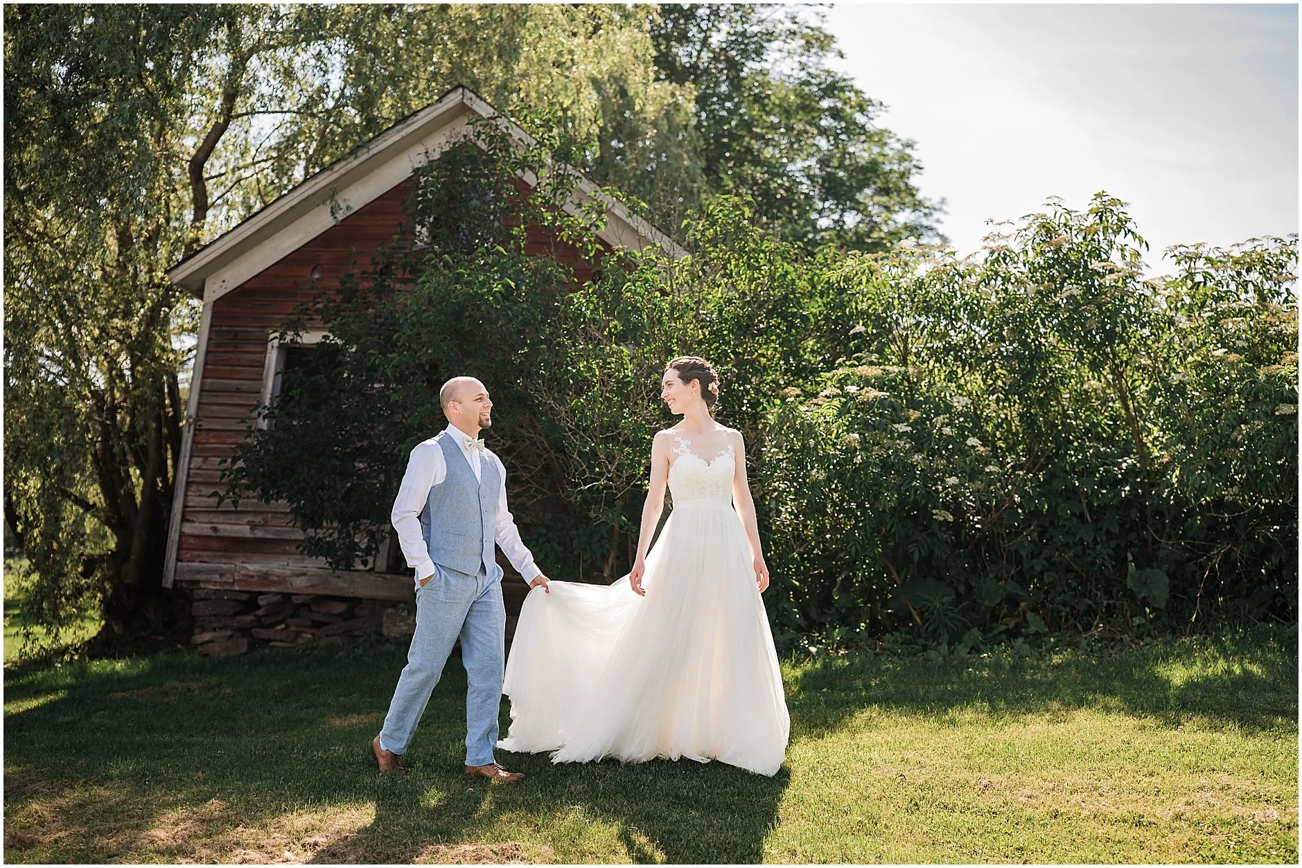 Groom holding the bride's dress as the newlyweds walk together as they explore the property of The Inn at West Settlement a wedding venue in the Catskill Mountains