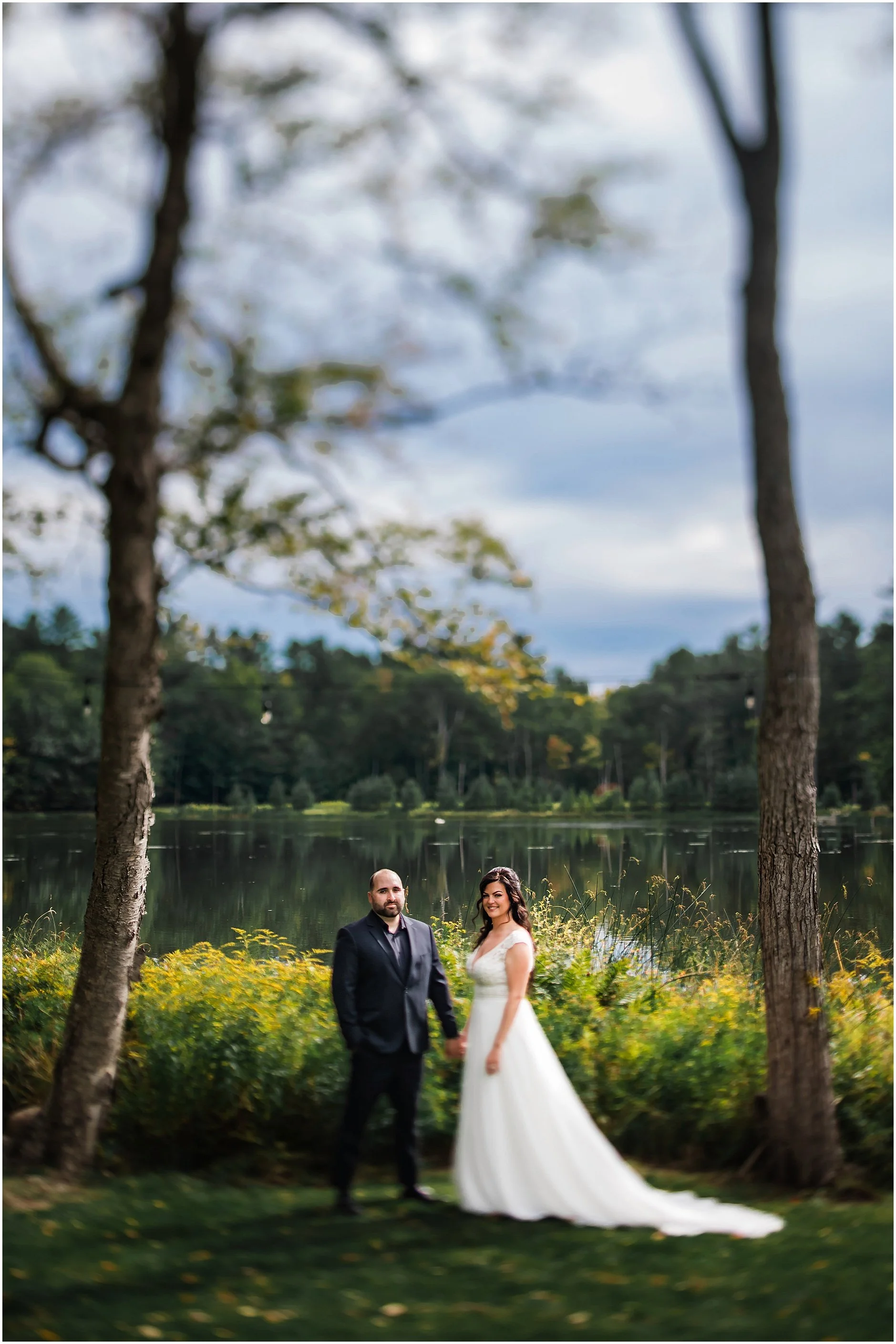 Timeless portrait of newlyweds by the water at The Rosemary at Spano Lake, a private wedding venue in Upstate New York