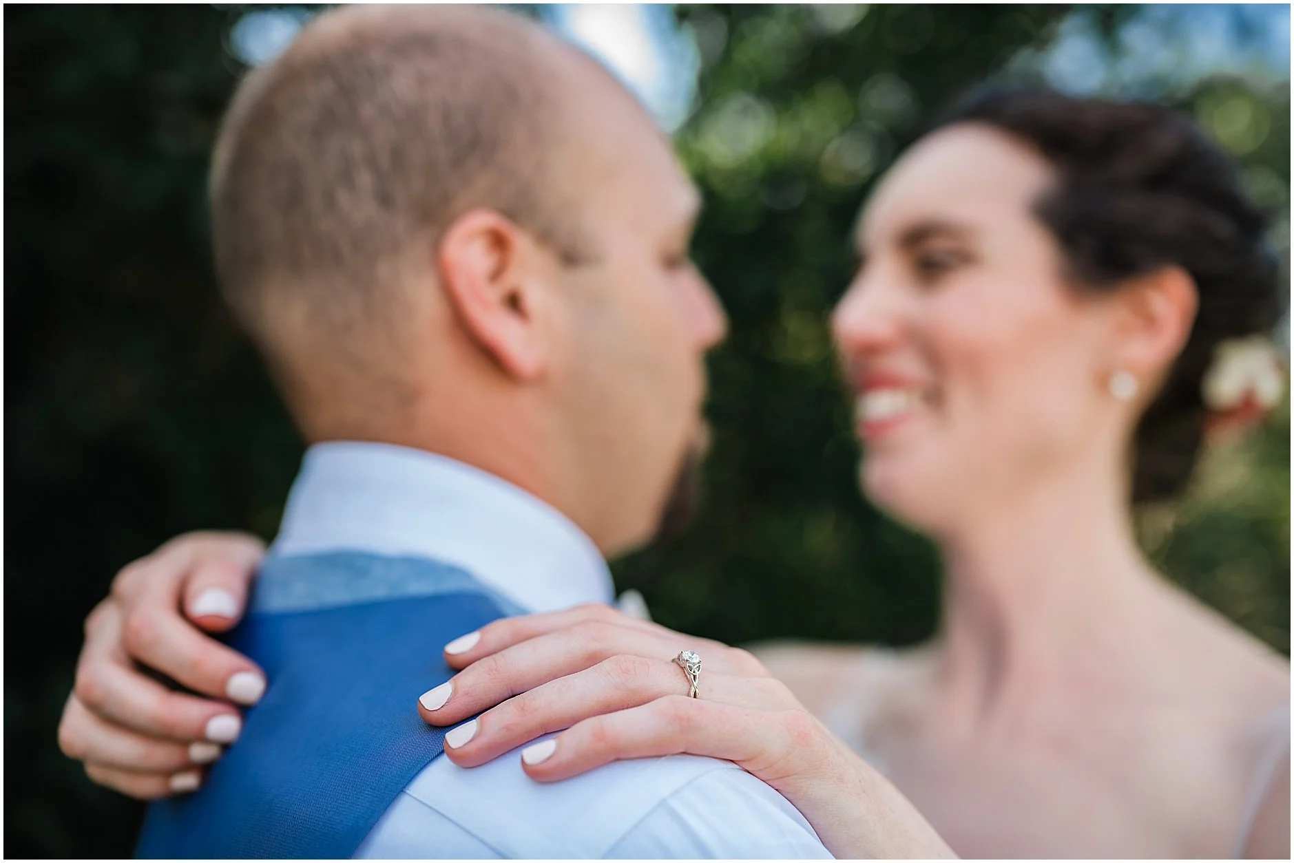 Bride and groom blurred out while the engagement ring is in focus