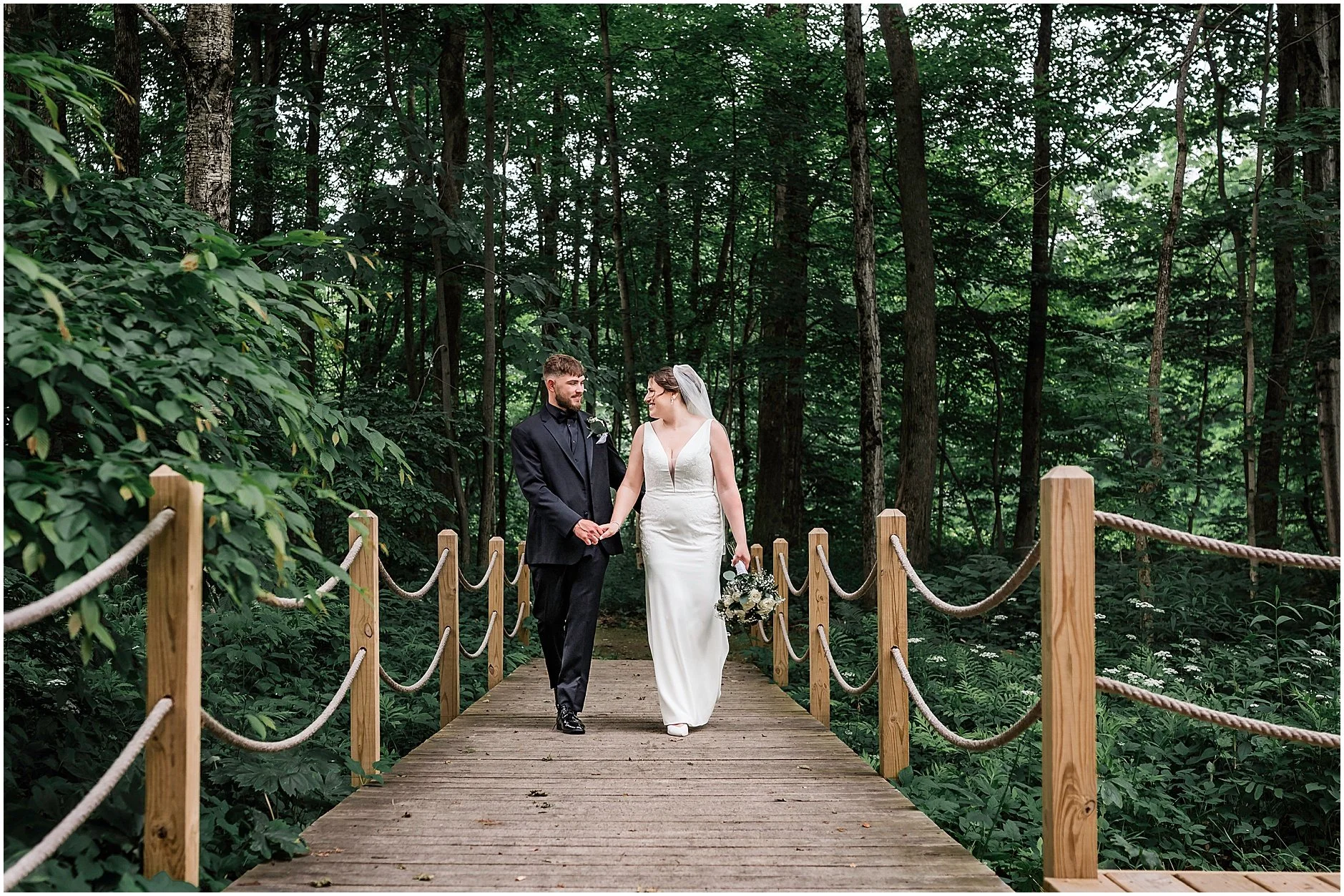 The bride and groom walking together surrounded by greenery at their wedding in the Catskills.