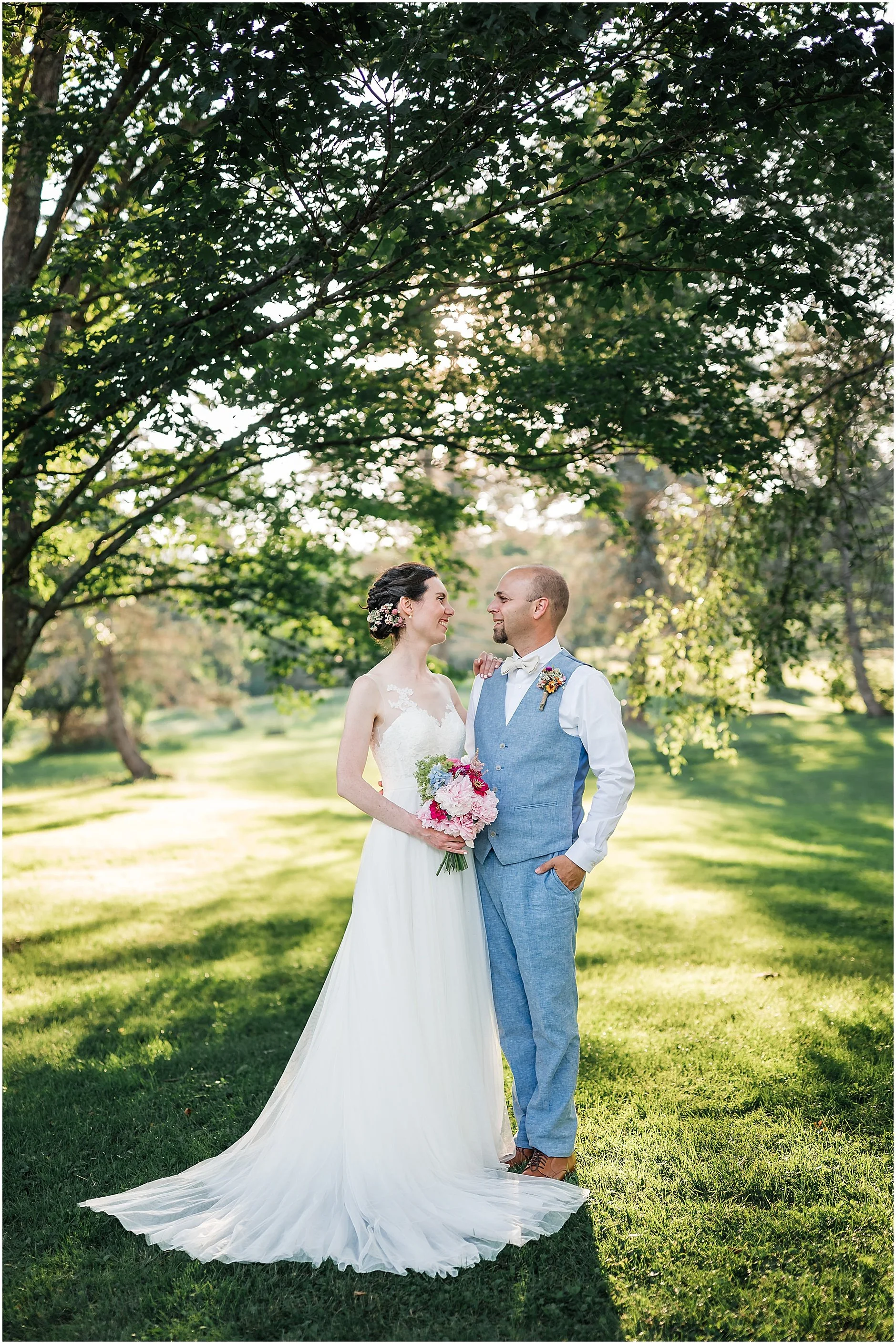 Classic bride and groom portrait under trees with golden light shinning through at The Inn at West Settlement