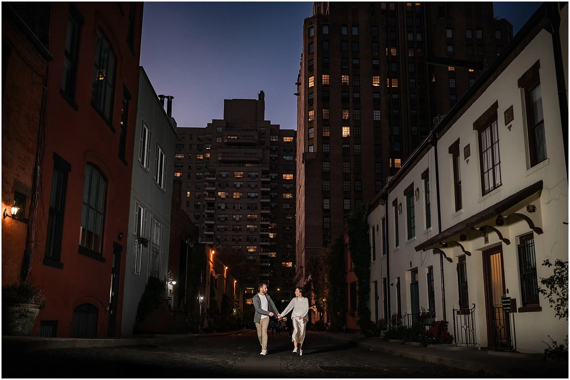 Engagement photos of couple running together holding hands down dark cobblestone street in Soho