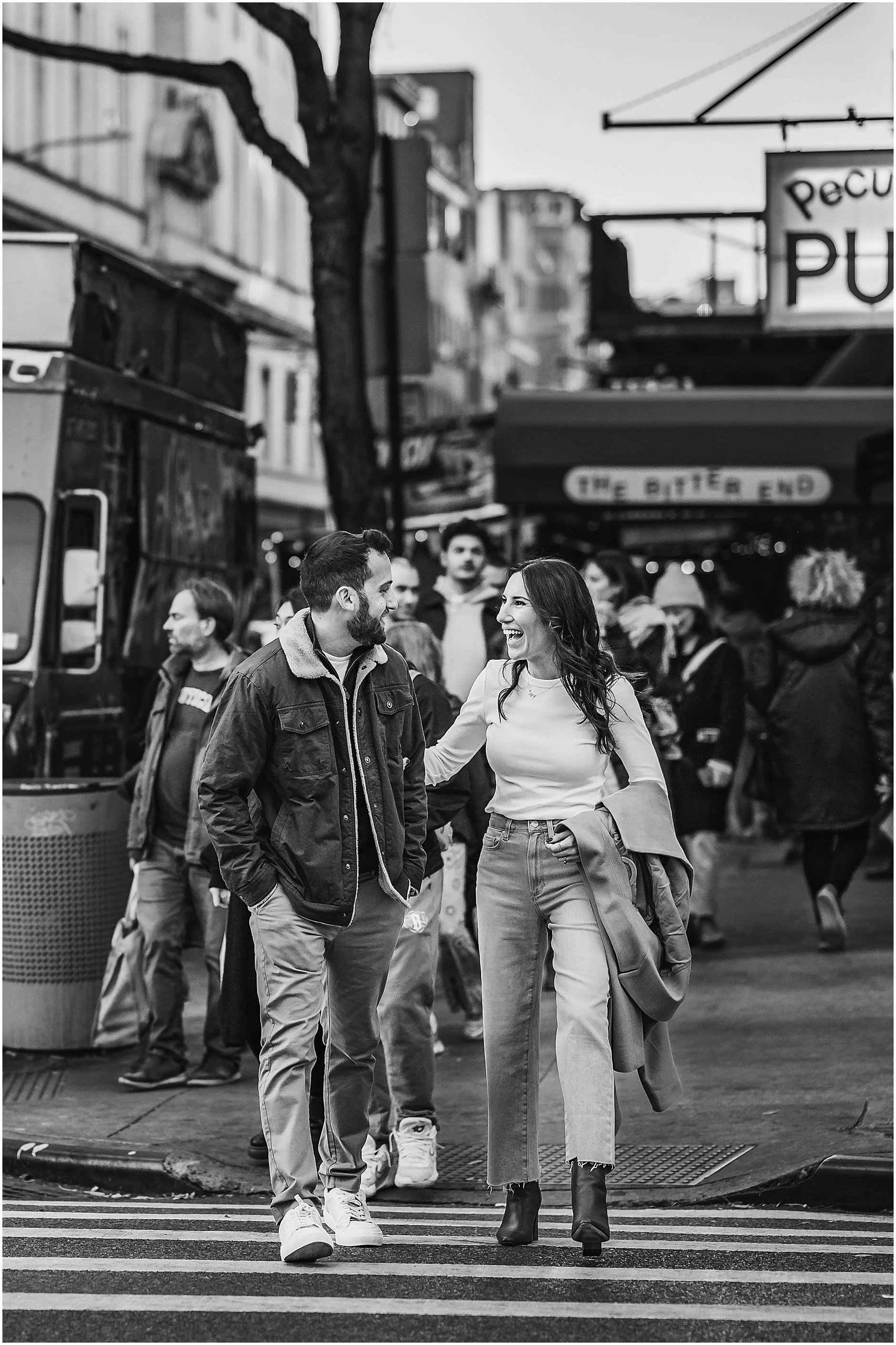 Candid black and white image of couple sharing a laugh as they walk across the street in Soho New York City