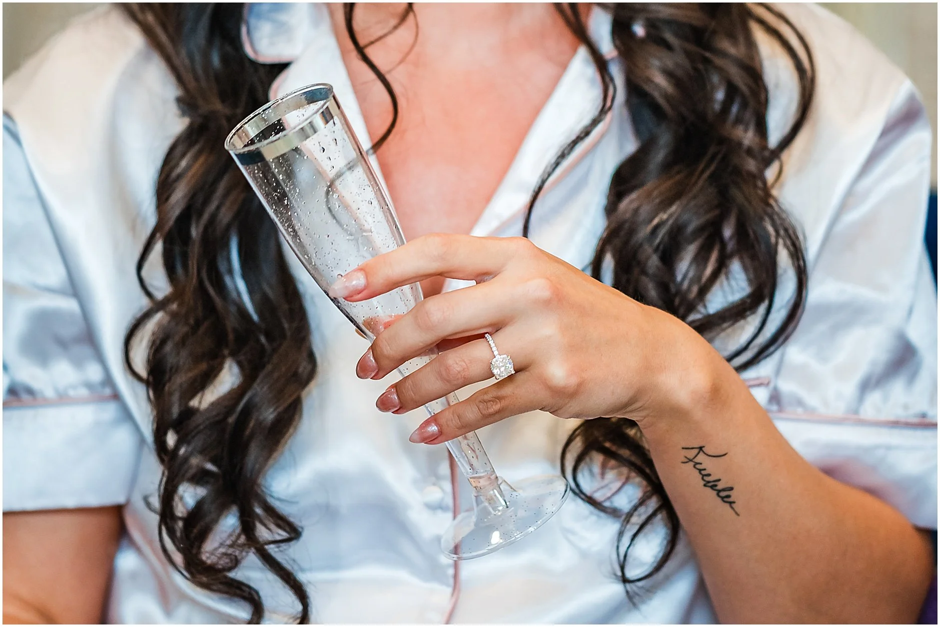 Bride holding glass of champagne showing off her engagement ring as she wears white pjs before her wedding ceremony in Cooperstown, New York