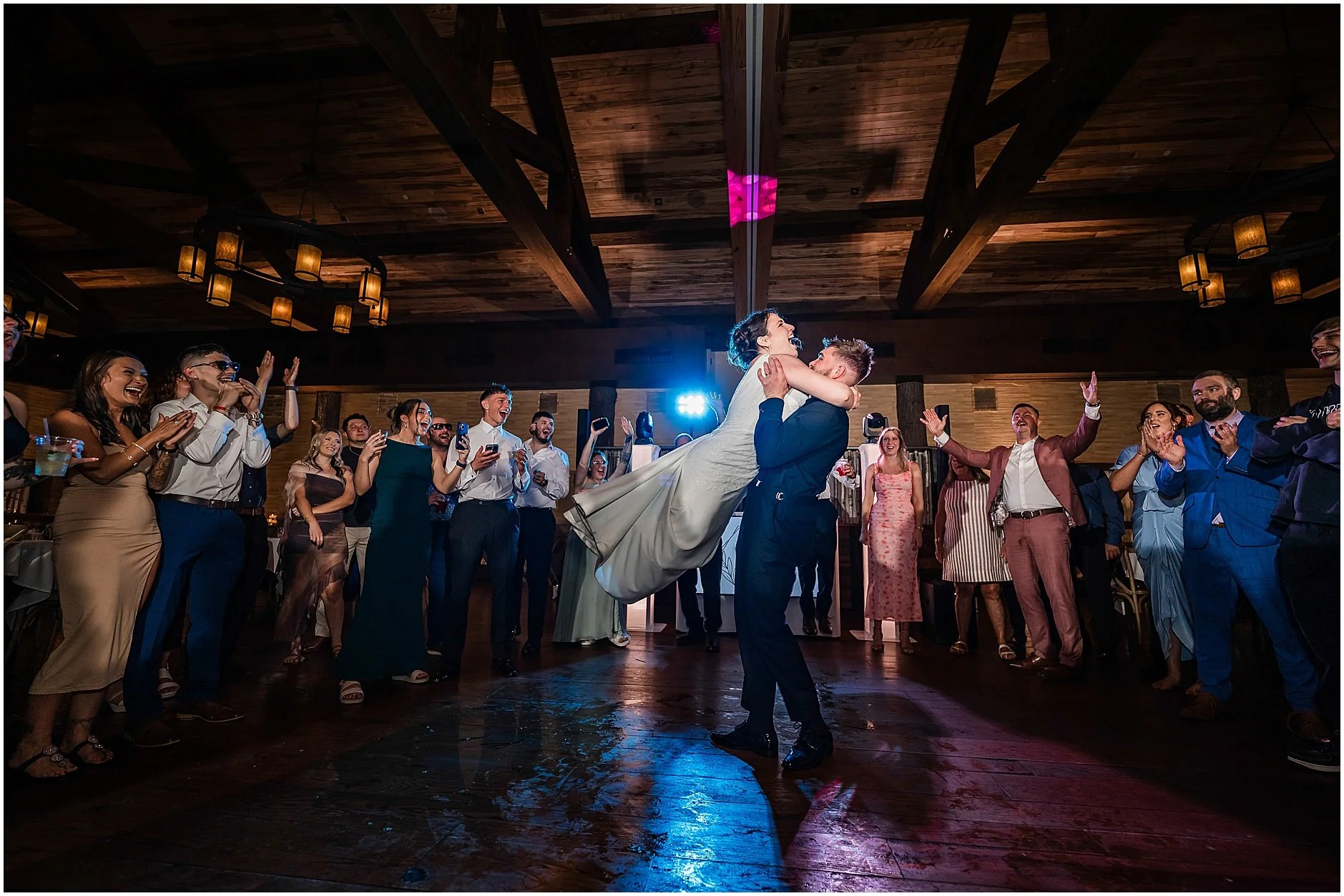Groom lifting his bride up in the air during their reception in New York with their loved ones surrounding them on the dance floor.